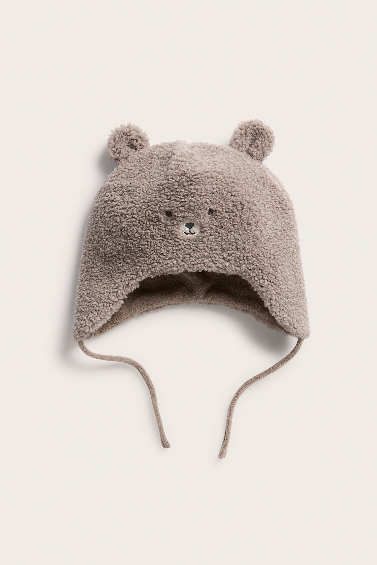 Edestä näkymä ruskeasta teddy-karhu-pilottipiposta, jossa korvaläpät ja nauhat.