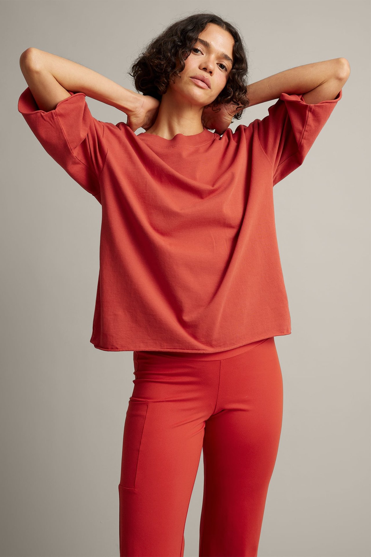 Framifrån, kvinna i löst sittande bränd orange t-shirt med breda ärmar och matchande smala byxor.