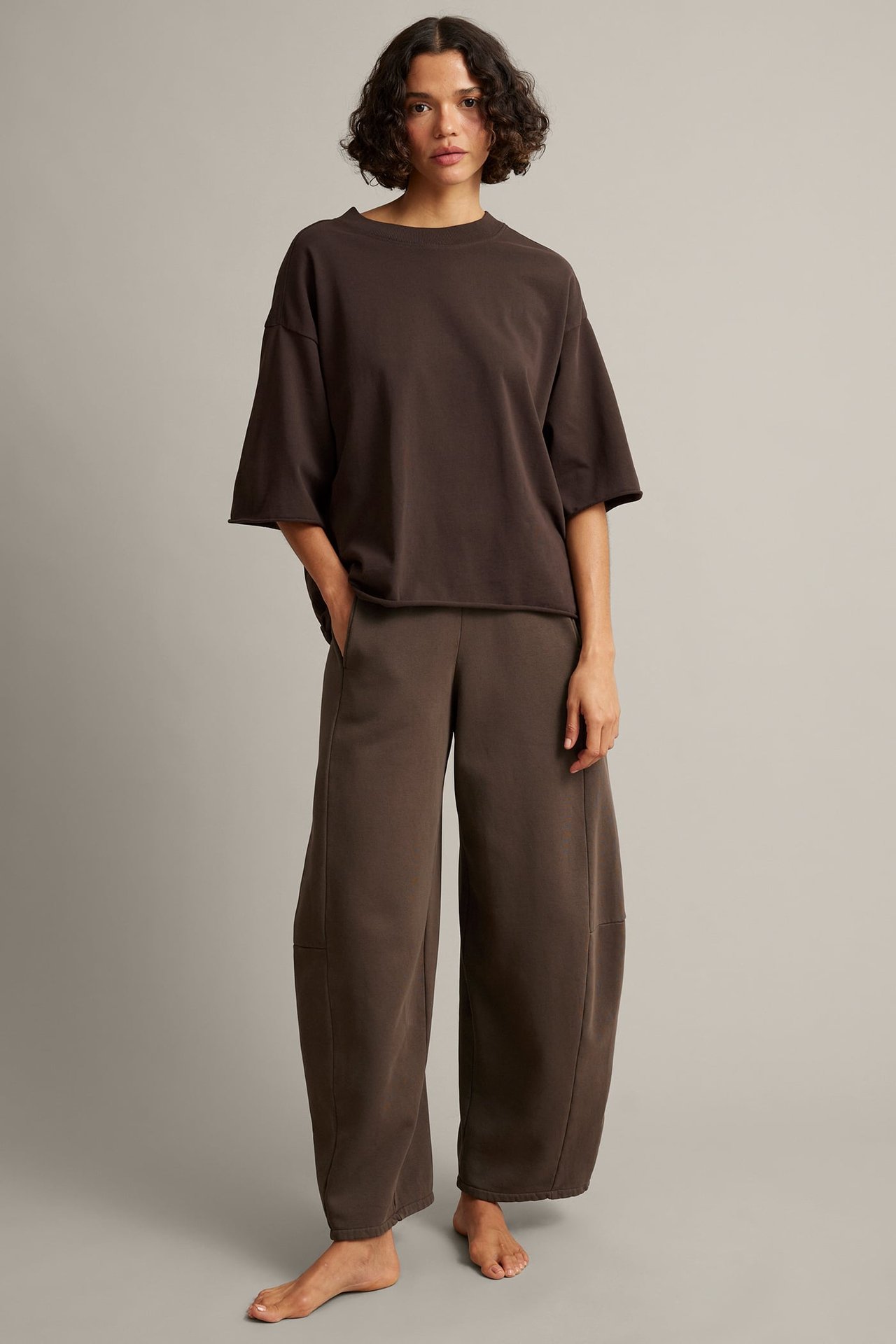 Framsida av kvinna i en mörkbrun, oversize kortärmad t-shirt och matchande vidbenta sweatpants.