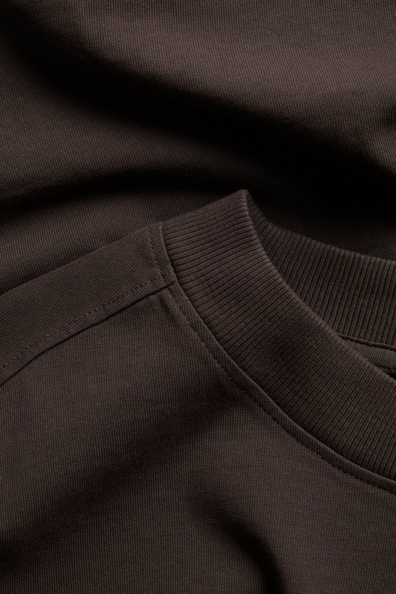 Närbild på en mörkbrun stickad sweatshirt med ribbad rundhals.