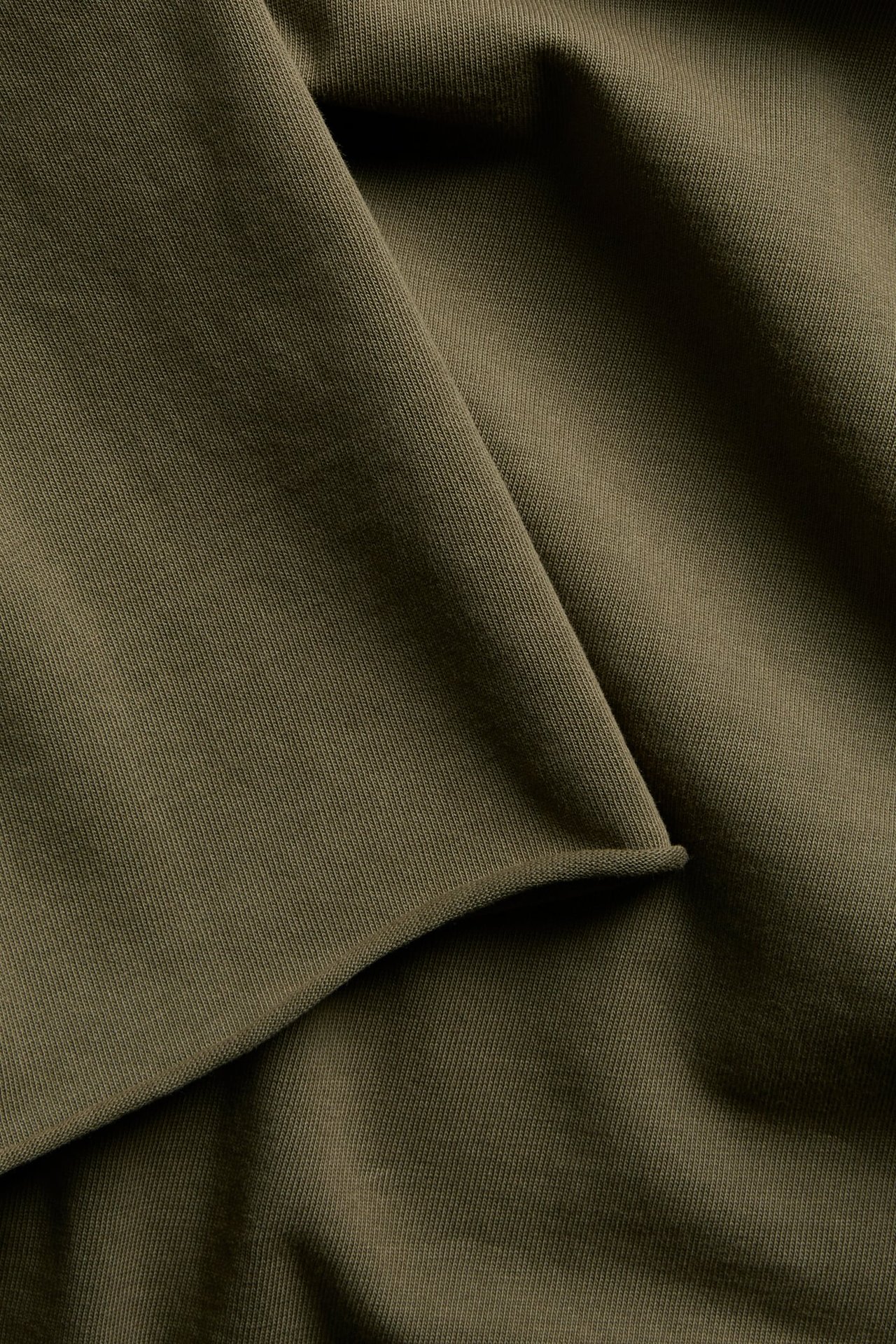 Närbild av olivgrönt ribbat stickat tyg, draperat och vikt.