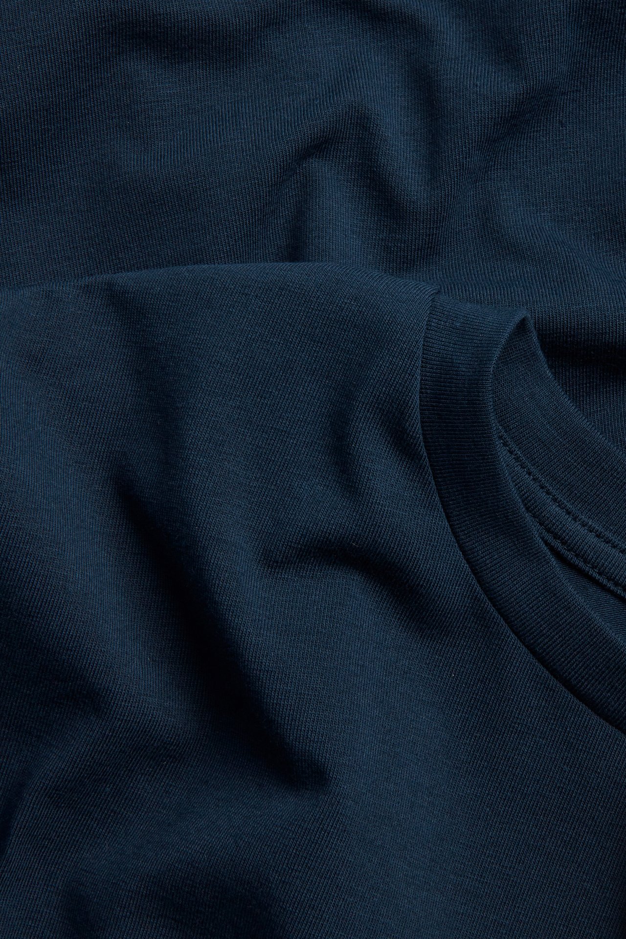 Lähikuva yksivärisestä tummansinisestä puuvillasekoitustopista, jossa näkyy ribbattu kangas ja osa pyöreästä kaula-aukosta.