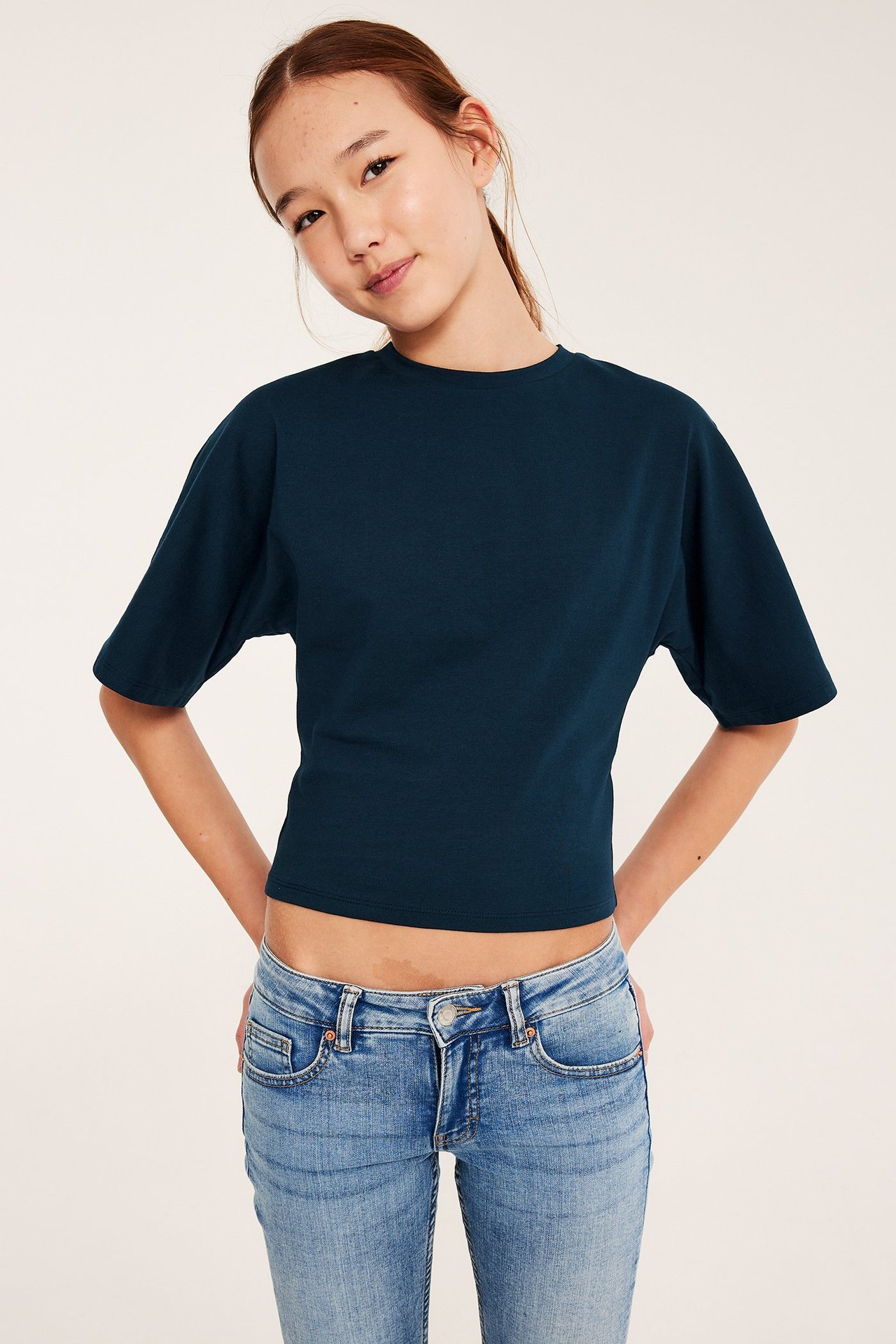 Kid i mörkblå kortärmad croppad topp med fjärilsärmar och ljusblå jeans, framifrån.