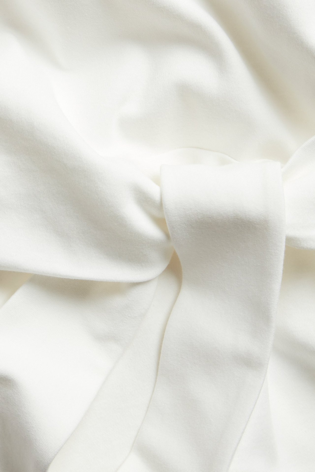 Närbild av en benvit kortärmad bomullstopp med synlig knytdetalj i midjan.