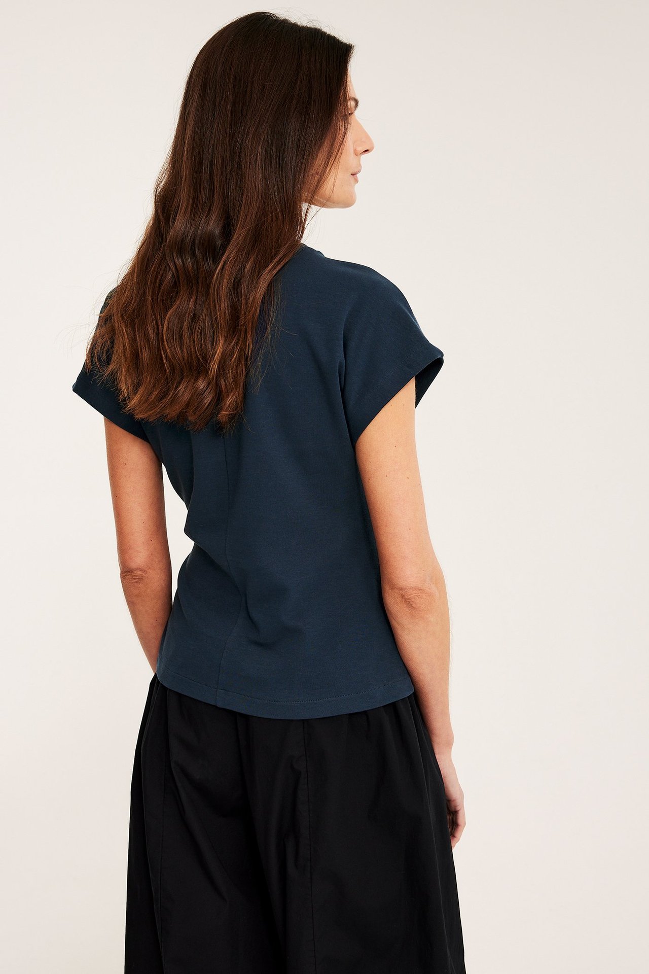 Widok z tyłu kobiety w granatowym bawełnianym topie z krótkimi podwiniętymi rękawami i czarnych szerokich spodniach.