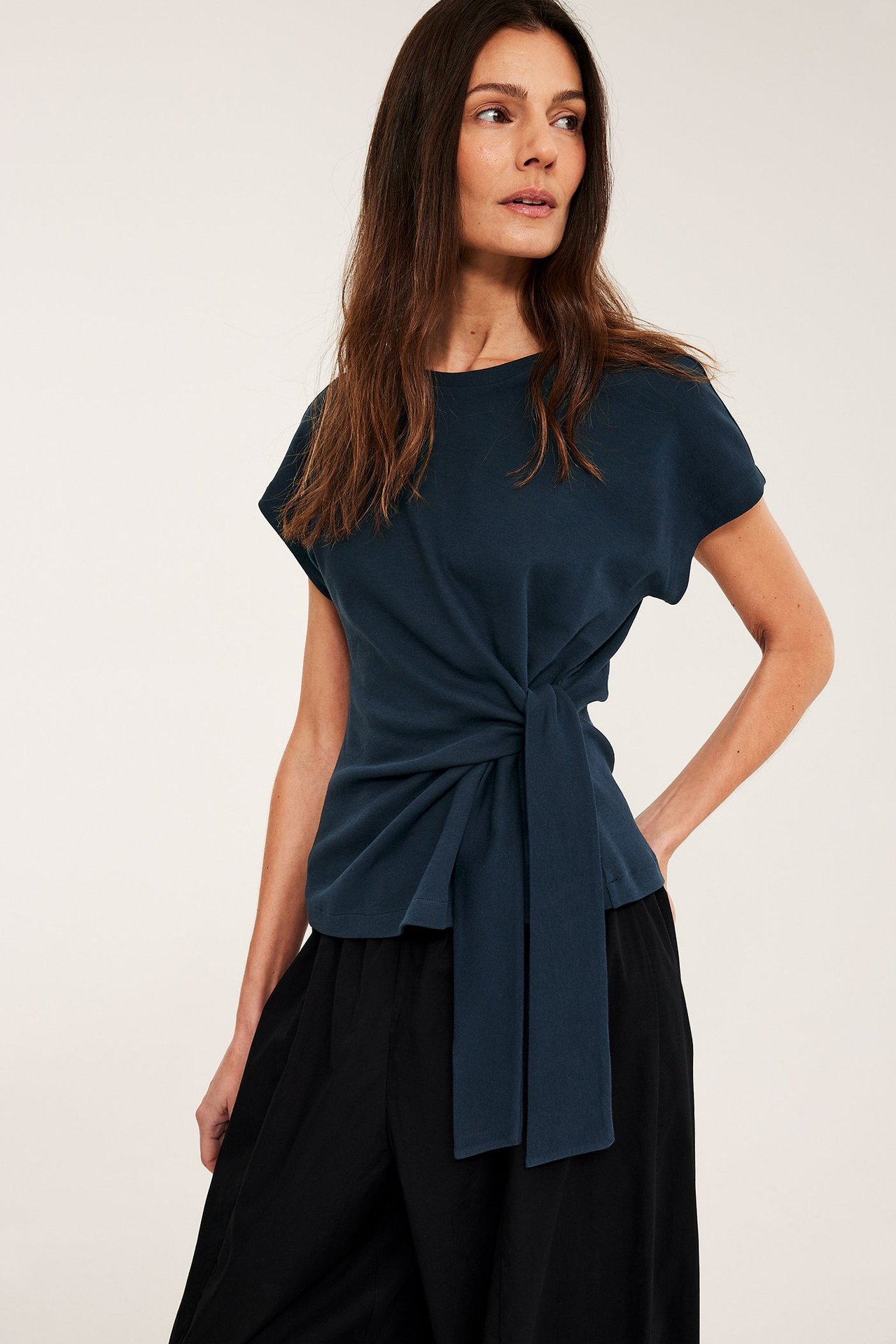 Widok z przodu: kobieta w granatowym bawełnianym topie z wiązaniem i czarnych szerokich spodniach.