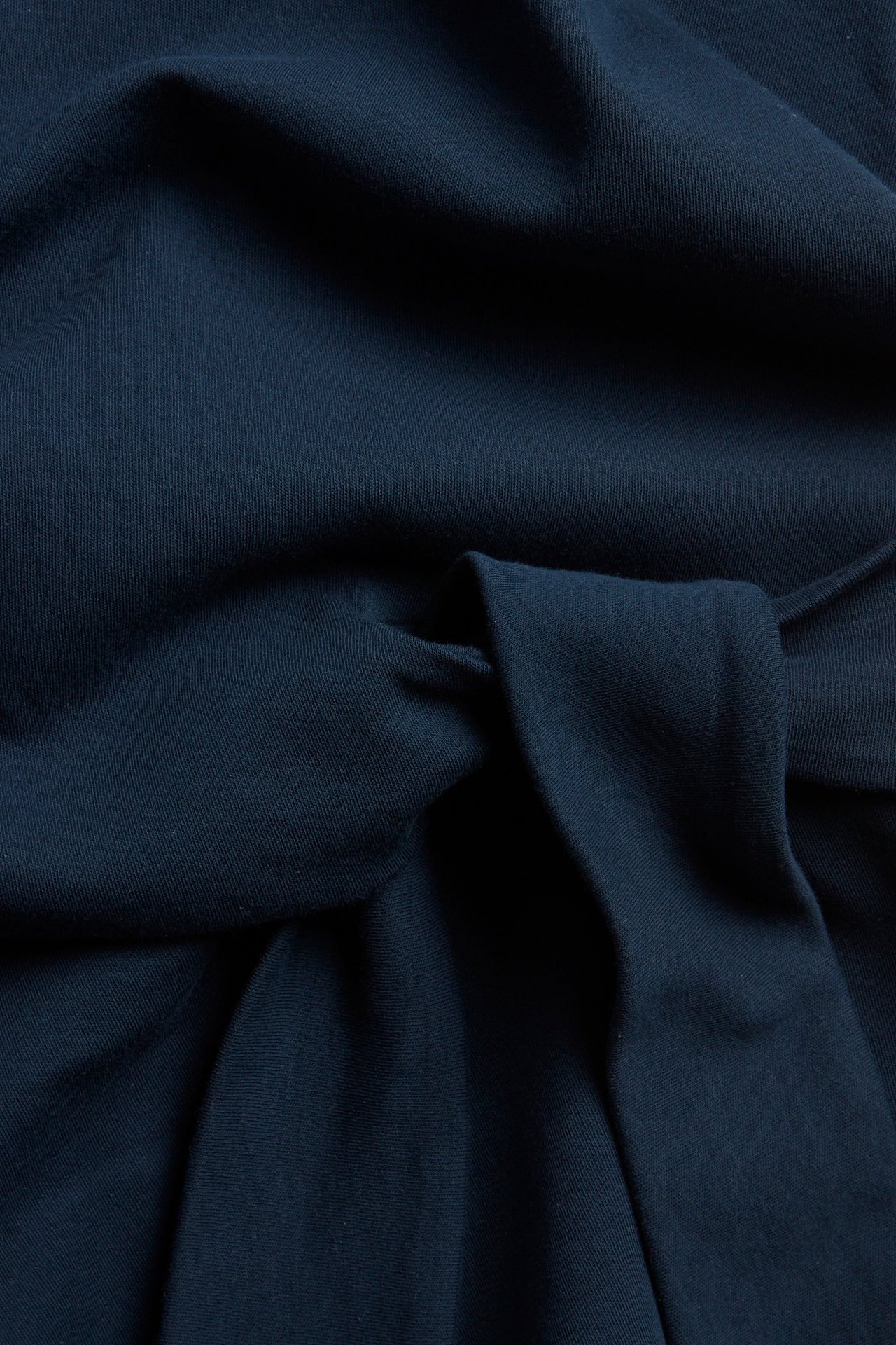 Närbild av mörkblå kortärmad bomullstopp med knytdetalj i midjan.