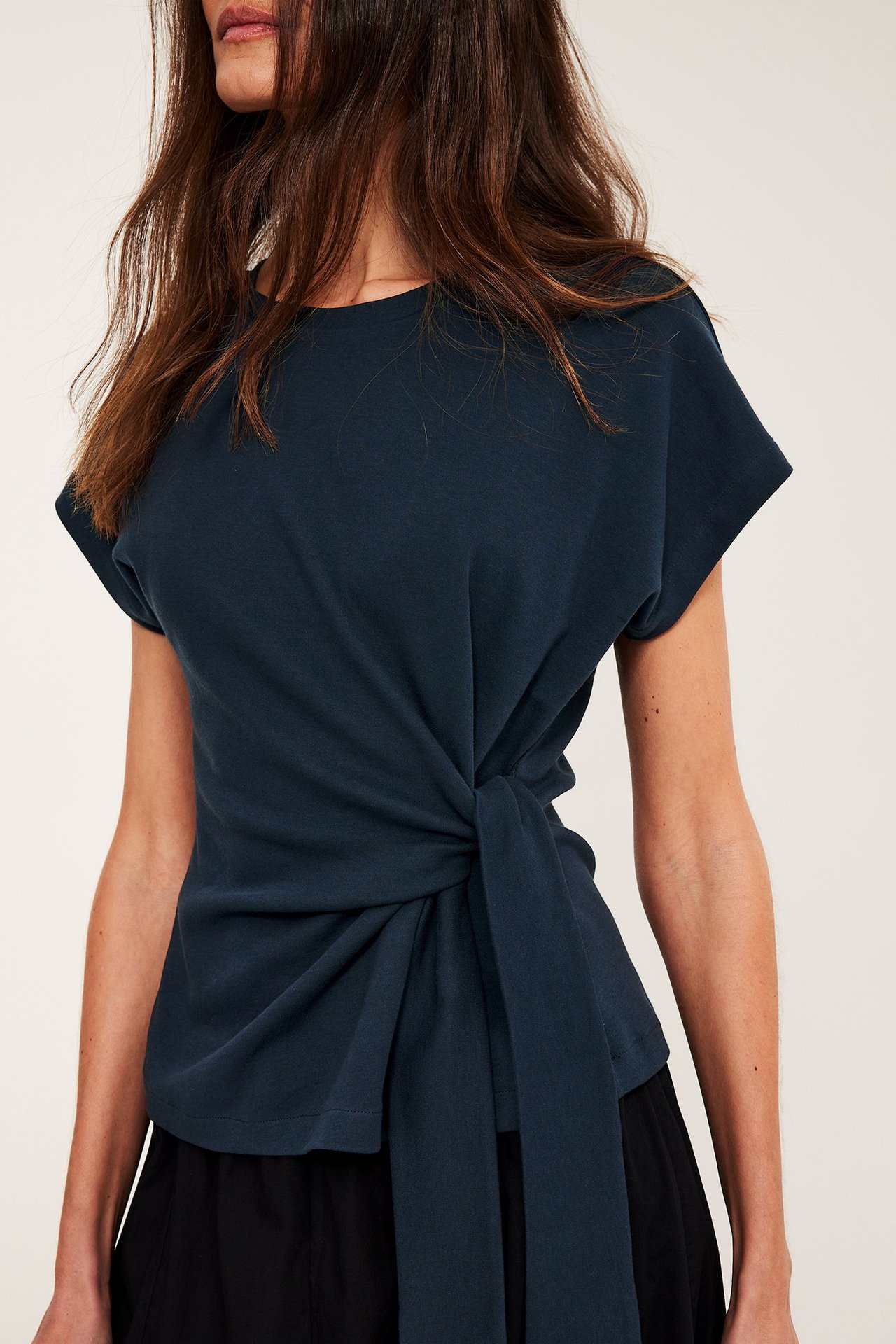 Front: Kobieta w ciemnoniebieskim bawełnianym topie z krótkim rękawem, wiązanym w talii, na spódnicy.