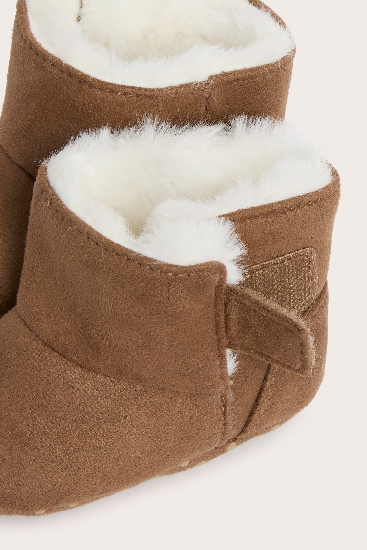 Närbild av bruna babyboots i fuskmocka med vitt fuskfoder och kardborreband.