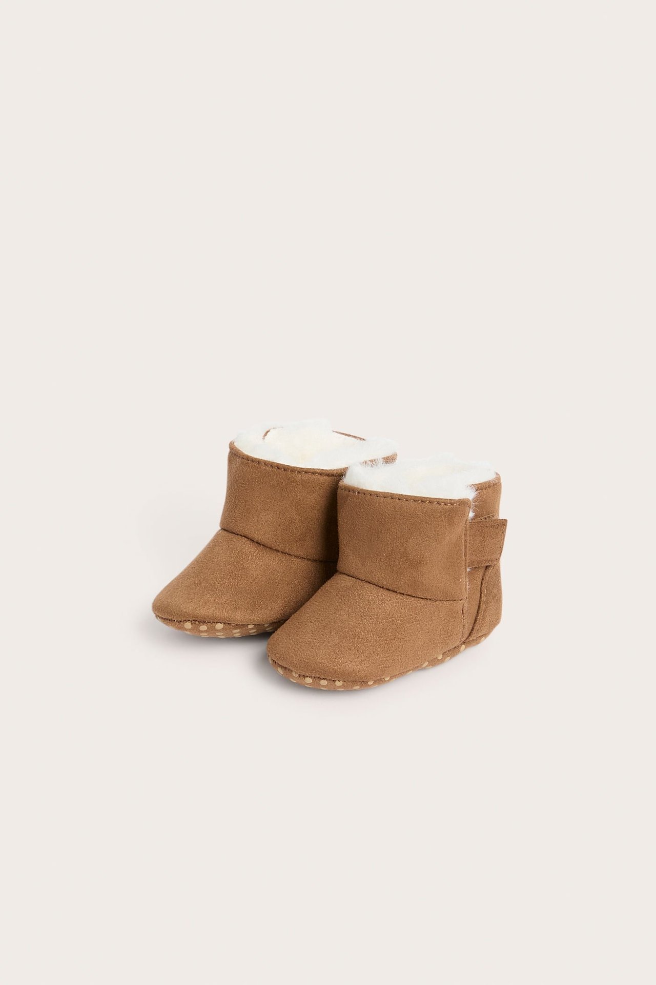 Brune babyboots i fuskemokka med hvitt fuskepelsfôr og prikkede såler, forfra.