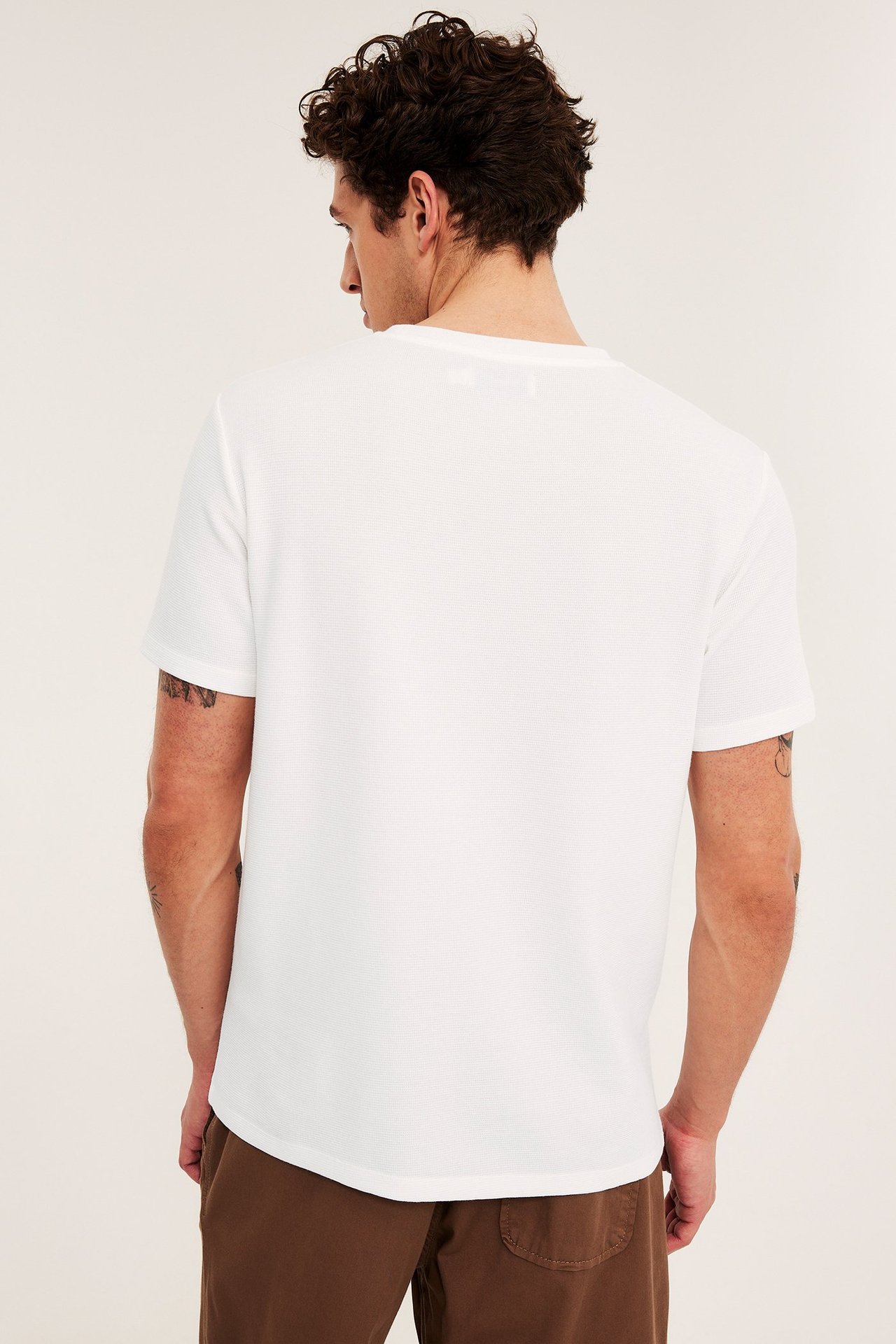 Bakfra, en mann i hvit teksturert regular fit t-skjorte og brune bukser.