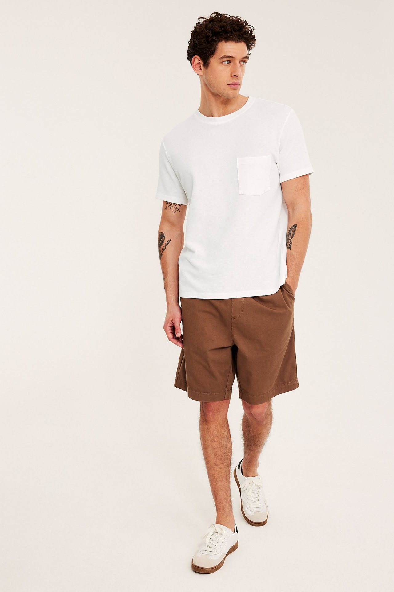 Frontbilde: mann i hvit strukturert t-skjorte med brystlomme, brune shorts og hvite sneakers.