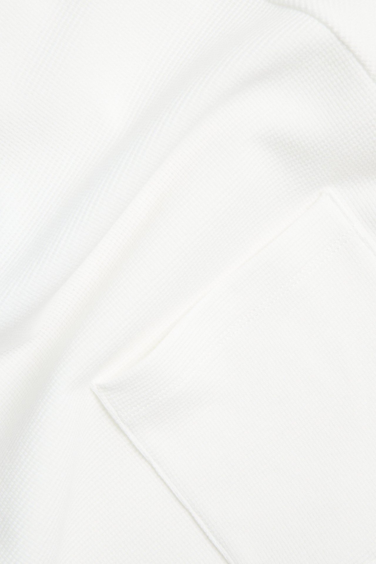 Lähikuva valkoisesta miesten t-paidasta, jossa on struktuurikuvio ja rintatasku.