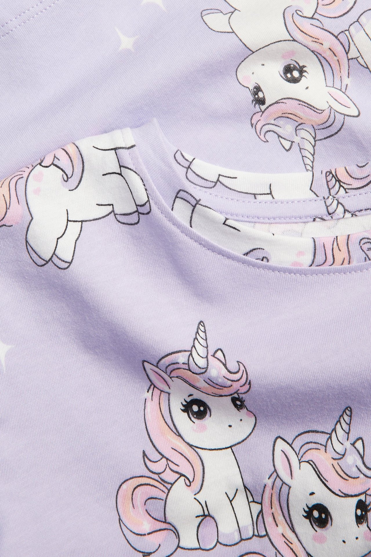 Zbliżenie na jasnofioletowy bawełniany top dziecięcy z uroczym wzorem jednorożców i gwiazd.