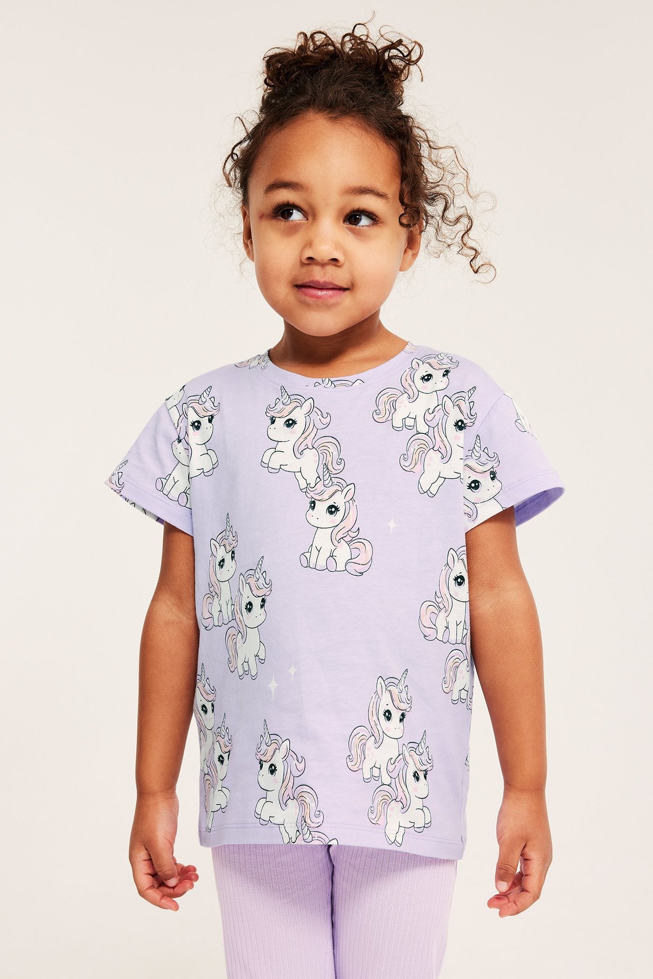 Framifrån: Flicka bär ljuslila bomullst-shirt med enhörningsprint och matchande ribbade leggings.