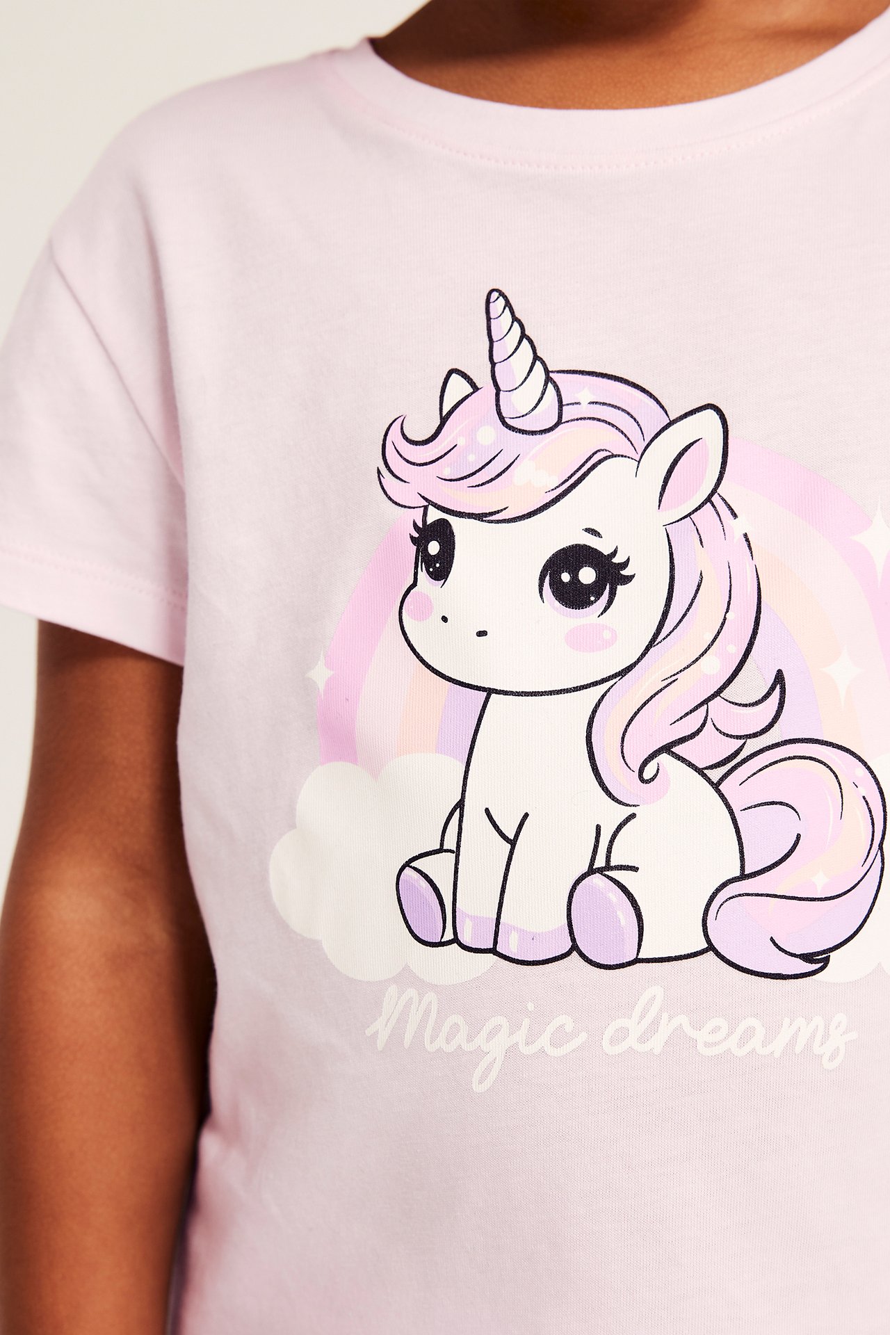 Närbild av en rosa barnt-shirt i bomull med enhörning, regnbåge och 'Magic dreams'-tryck.
