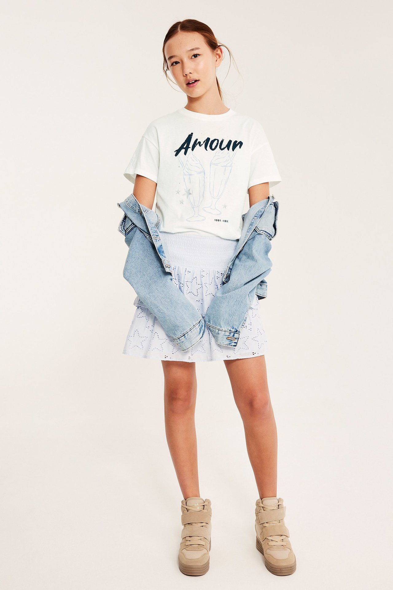 Frontvisning: Barn i offwhite T-skjorte med 'Amour'-trykk, blå dongerijakke, hvit skjørt og beige sko.