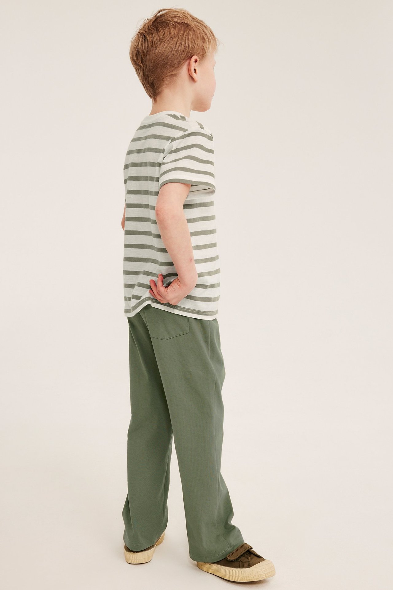 Sivukuva lapsesta yllään tummanvihreät suoralahkeiset collegehousut ja raidallinen t-paita.