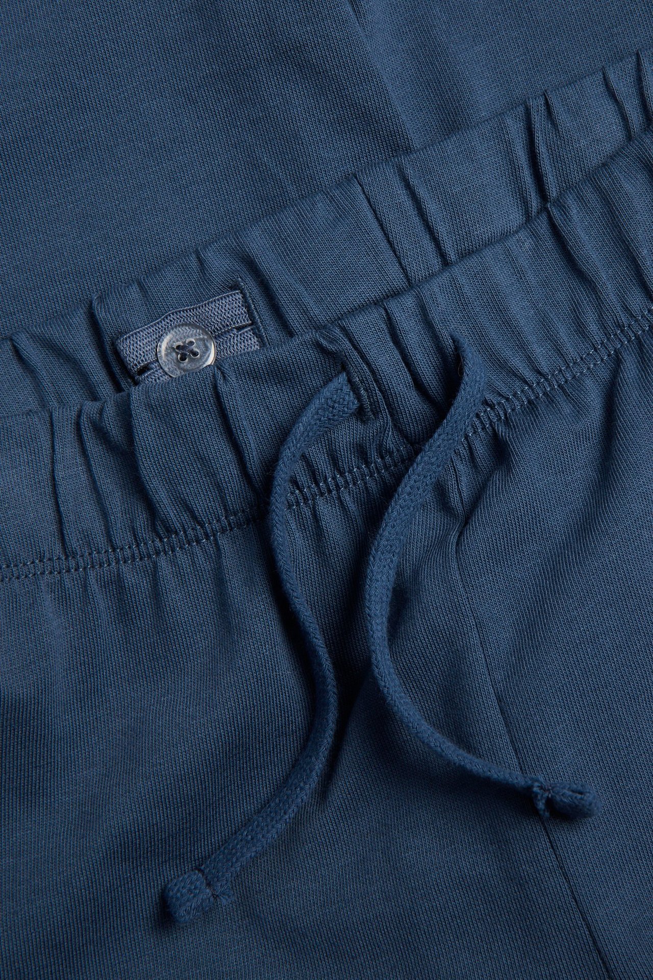Zbliżenie na niebieskie bawełniane spodnie dresowe, elastyczny pas ze sznurkiem i regulowanym guzikiem.