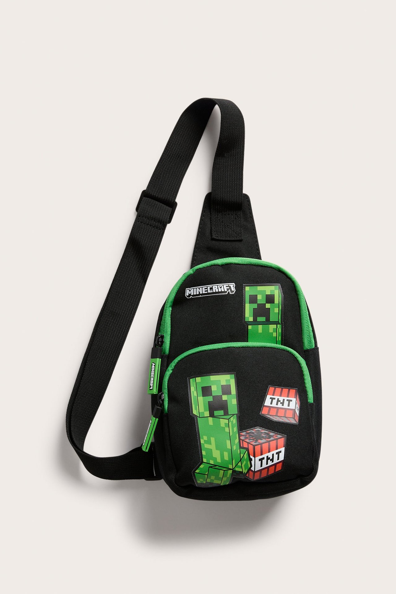 Edestä, musta Minecraft-olkalaukku vihreällä reunuksella, Creeper-hahmoilla ja TNT-lohkoilla.