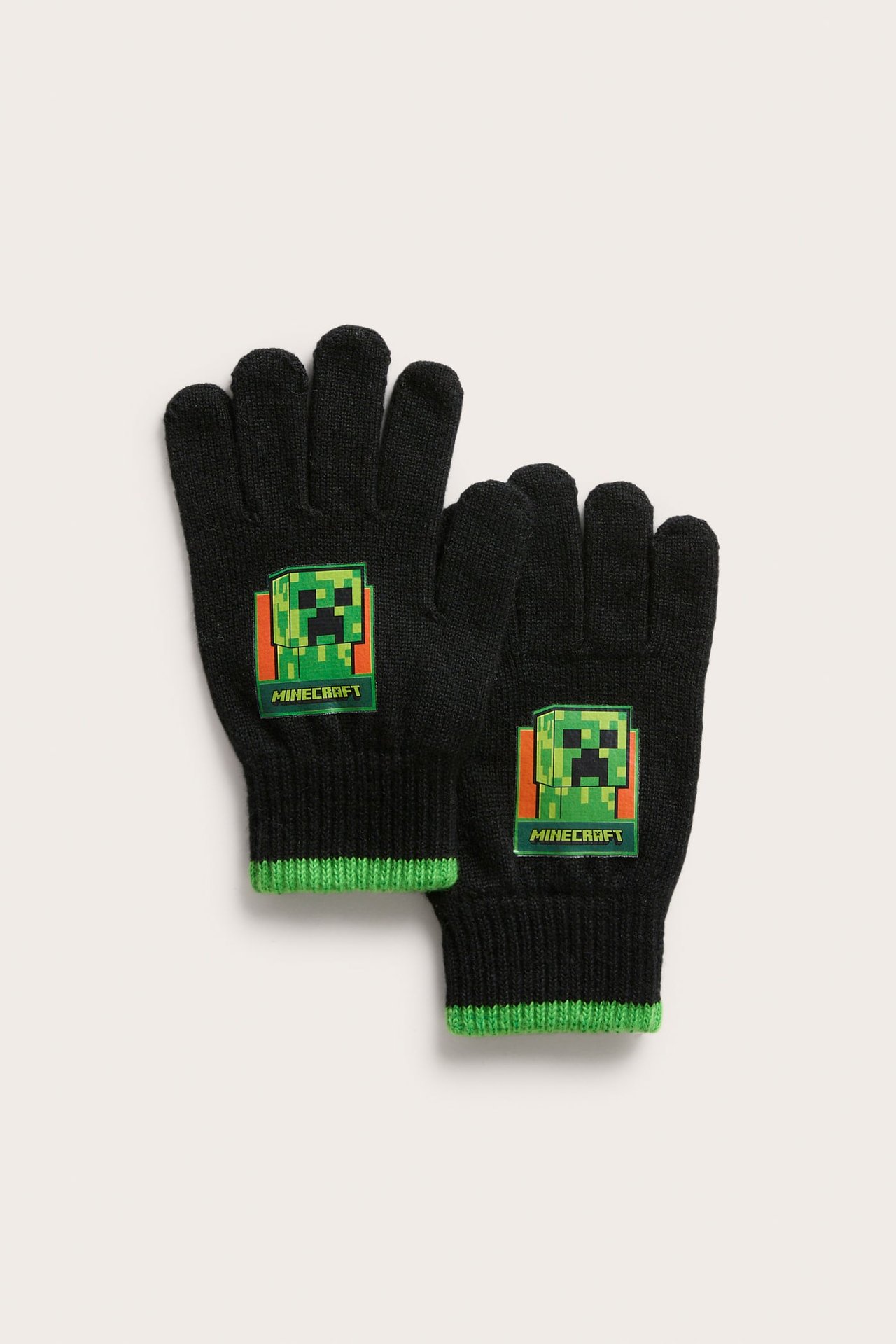 Płasko ułożone dwie czarne dzianinowe rękawiczki z zielonymi mankietami i wzorem Minecraft Creeper.