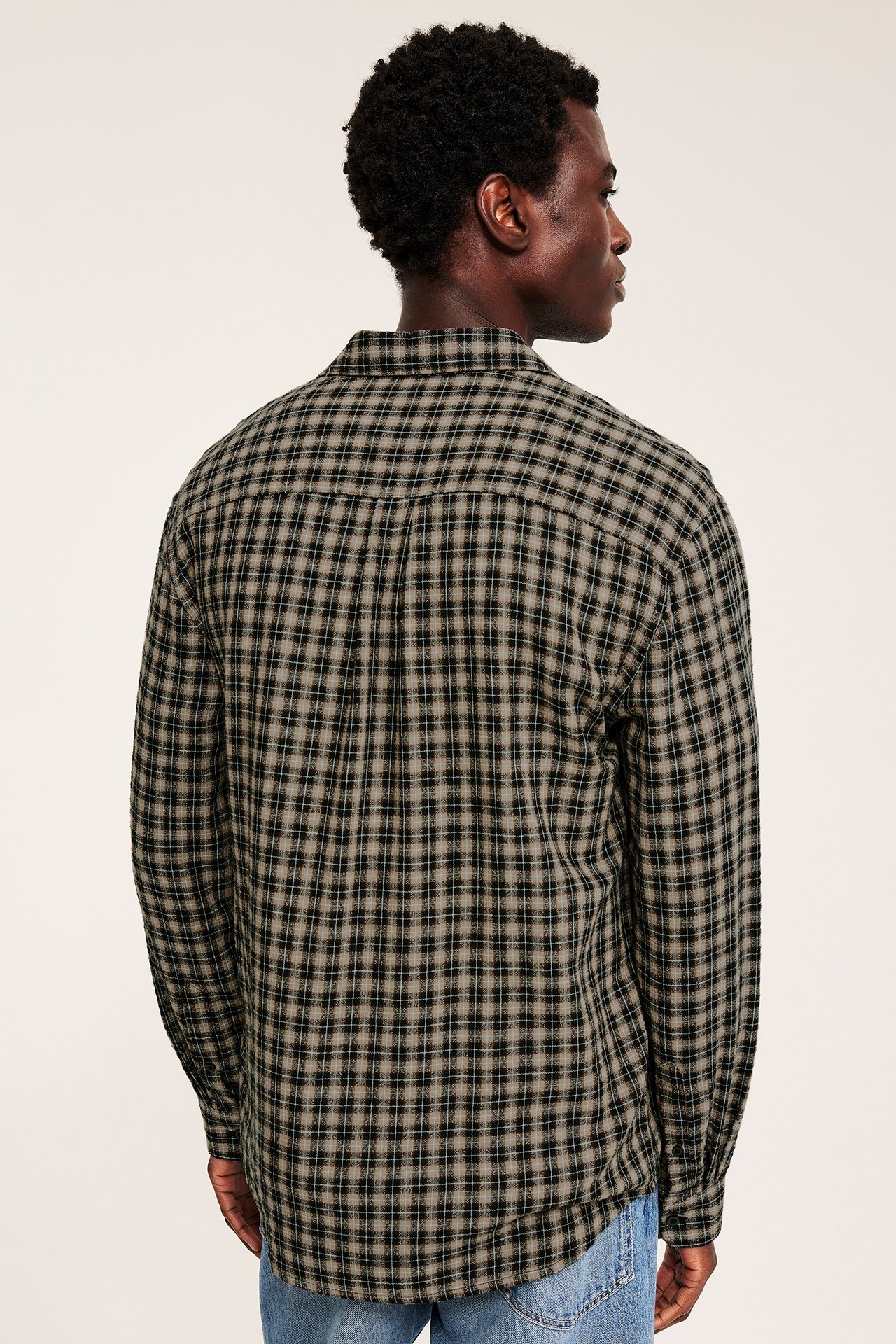 Voksen mann, bakre høyre sidevisning, med svart-beige rutete langermet skjorte og blå jeans.