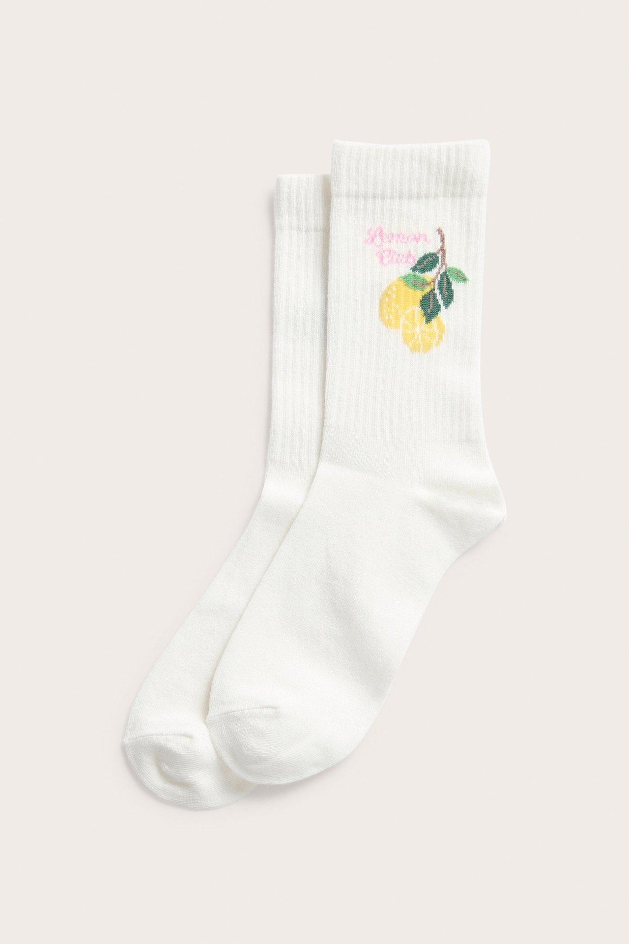 Edestä nähtynä valkoiset ribbireunatut sukat, joissa keltainen sitruunakuvio ja pinkki 'Lemon Drop' -teksti.