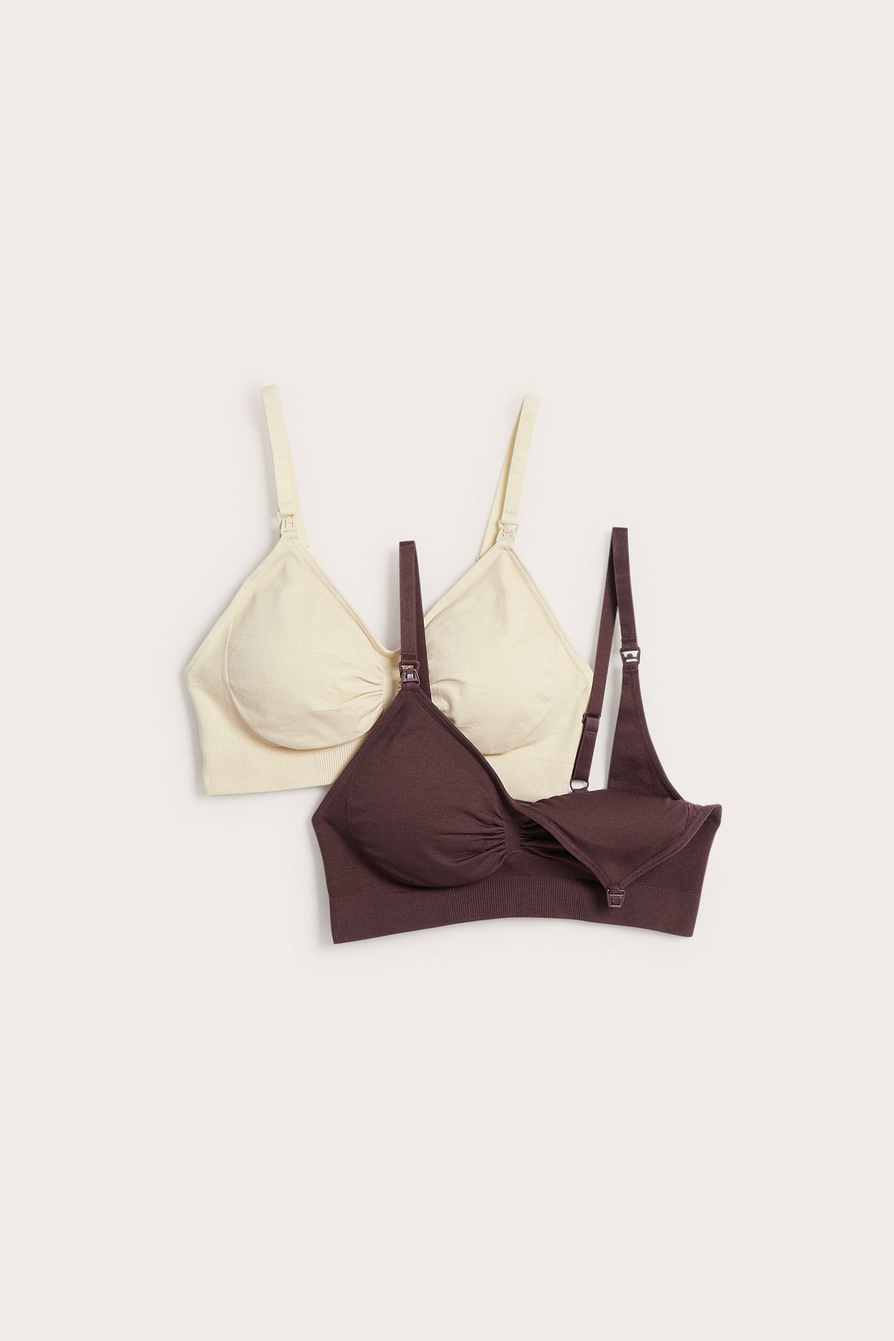 Flat lay av to sømløse amme-BH-er, en mørk brun med åpen cup og en lys beige.