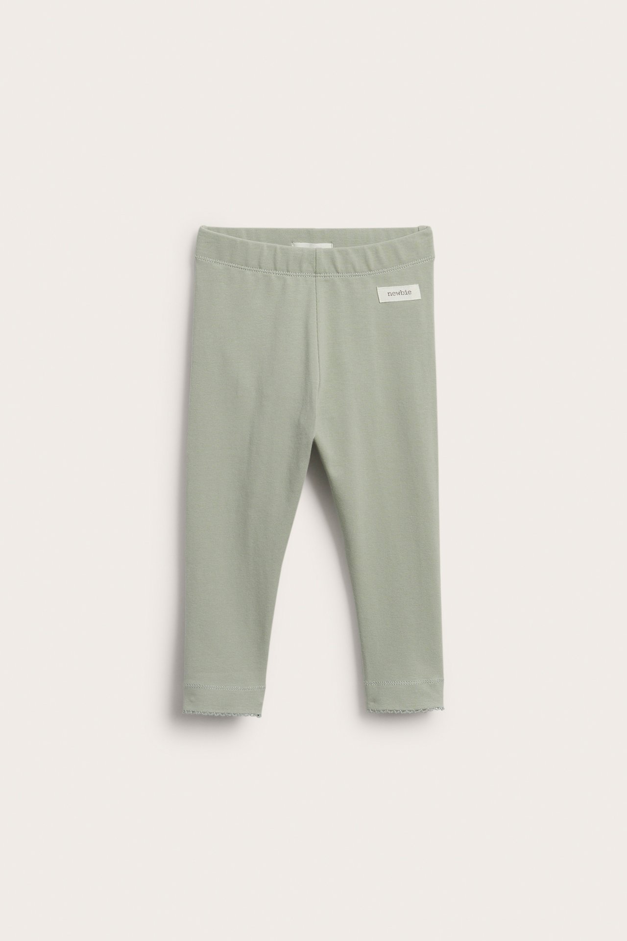 Frontvy av babyleggings i ljusgrön bomull med resårmidja och vågiga ankelkanter.
