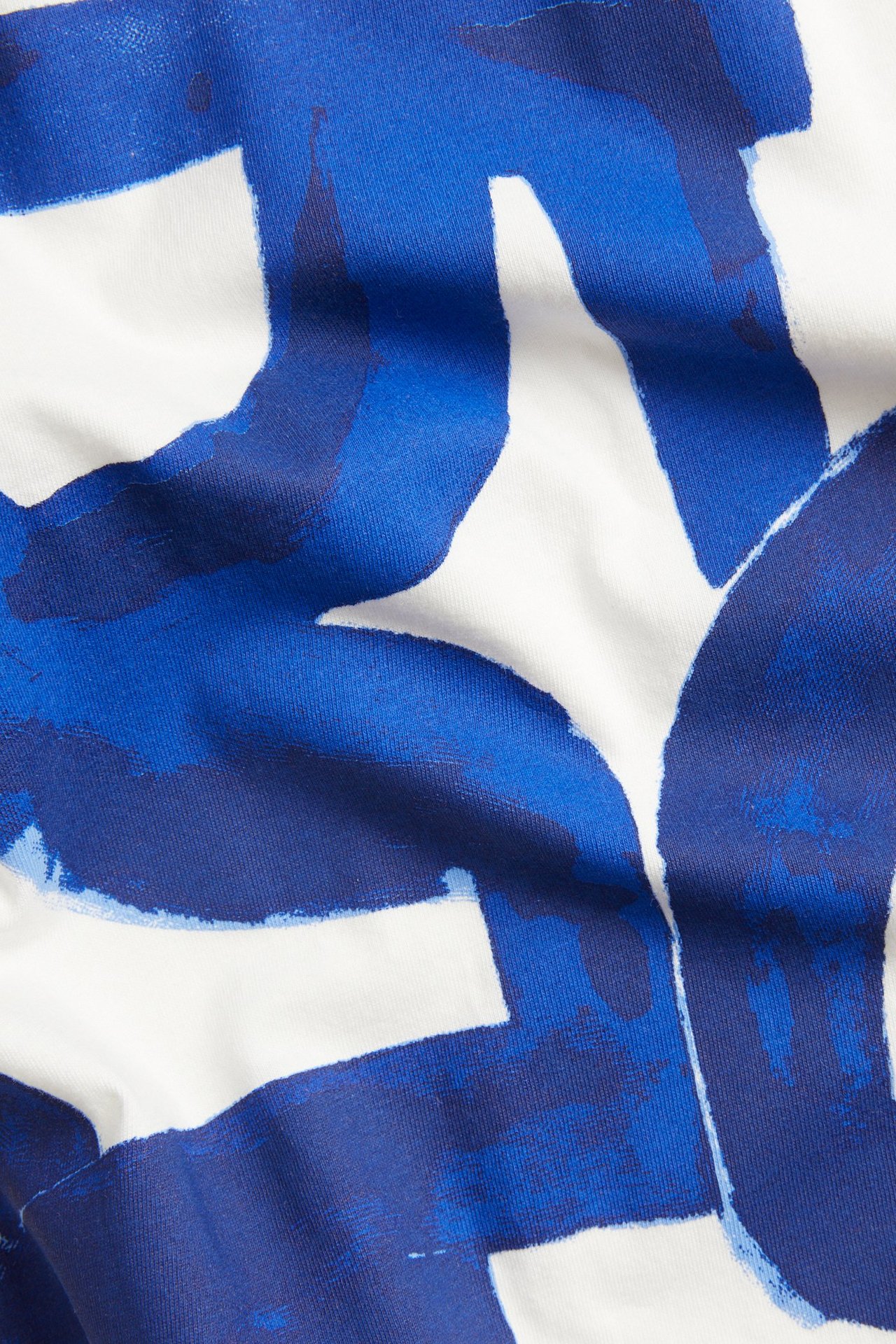 Nærbilde av en hvit bomulls-t-skjorte med et dristig blått abstrakt fronttrykk.