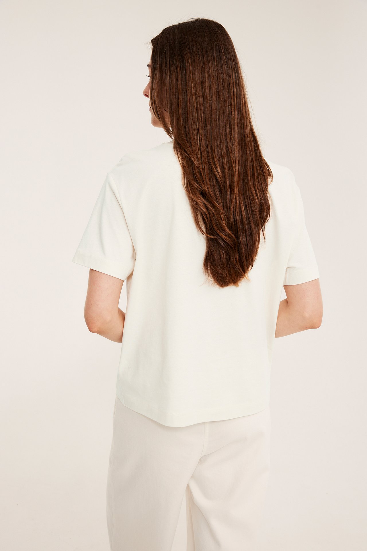 Bakifrån, en kvinna i en offwhite bomulls-t-shirt och offwhite byxor.