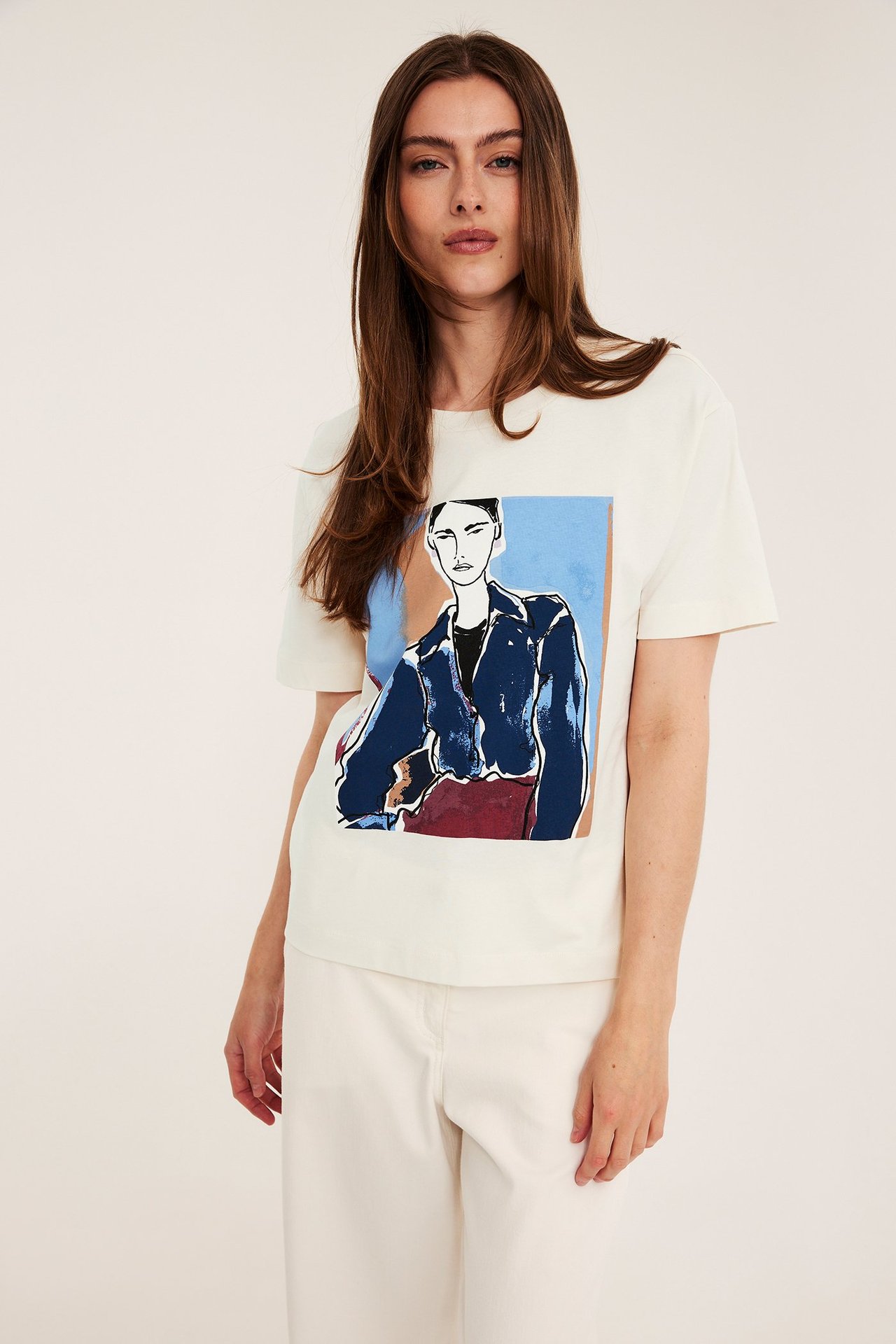 Forfra: Kvinne i offwhite bomulls-T-skjorte med illustrert trykk, stylet med offwhite bukser.