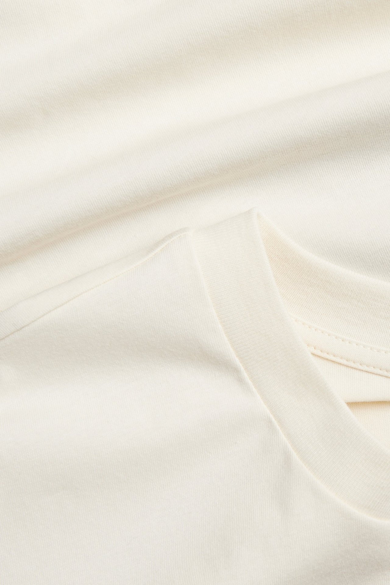 Nærbilde av en naturhvit bomulls-t-skjorte, viser stoffet og halslinningen.
