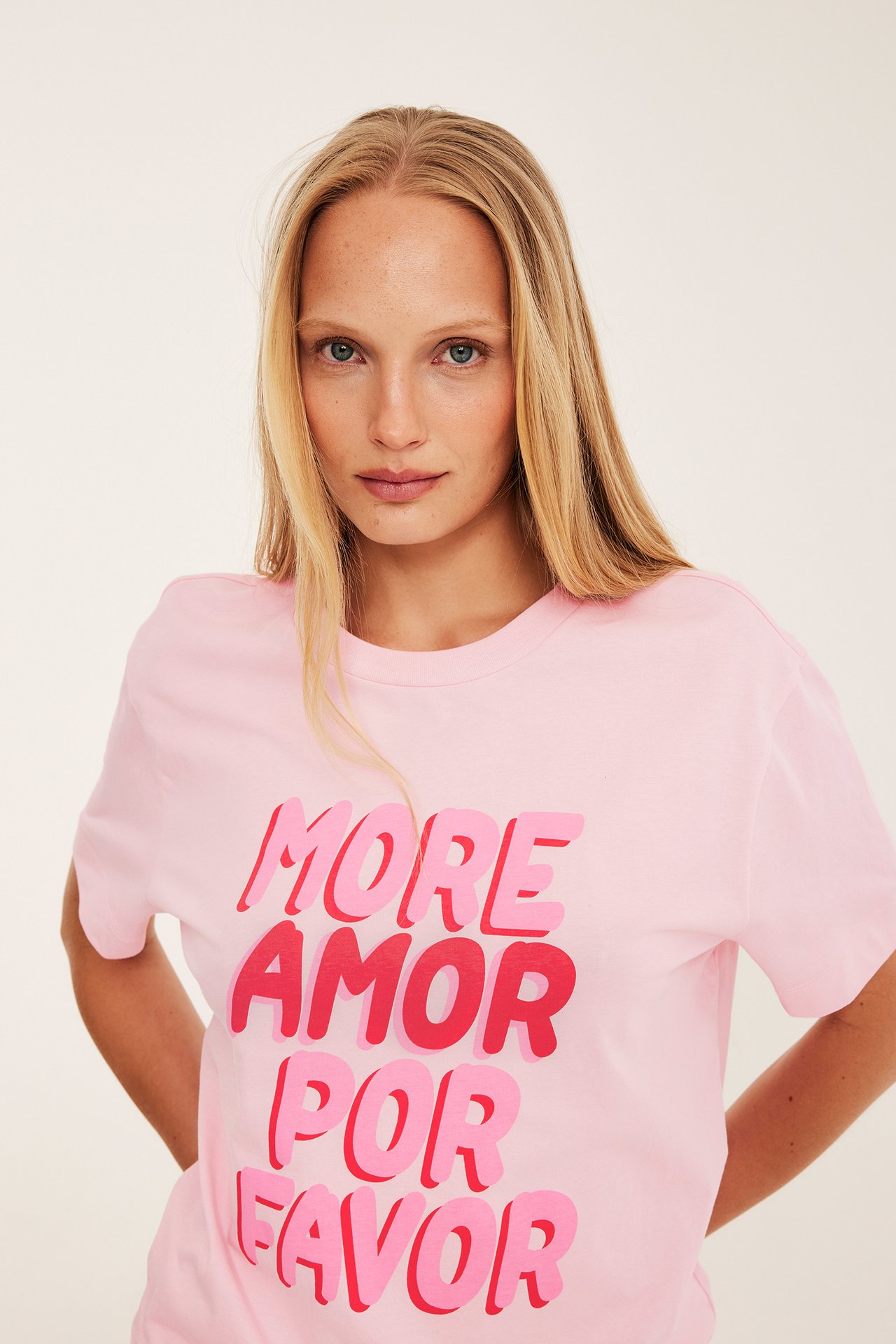 Framifrån, kvinna i rosa bomulls-t-shirt med "More amor por favor" tryck.