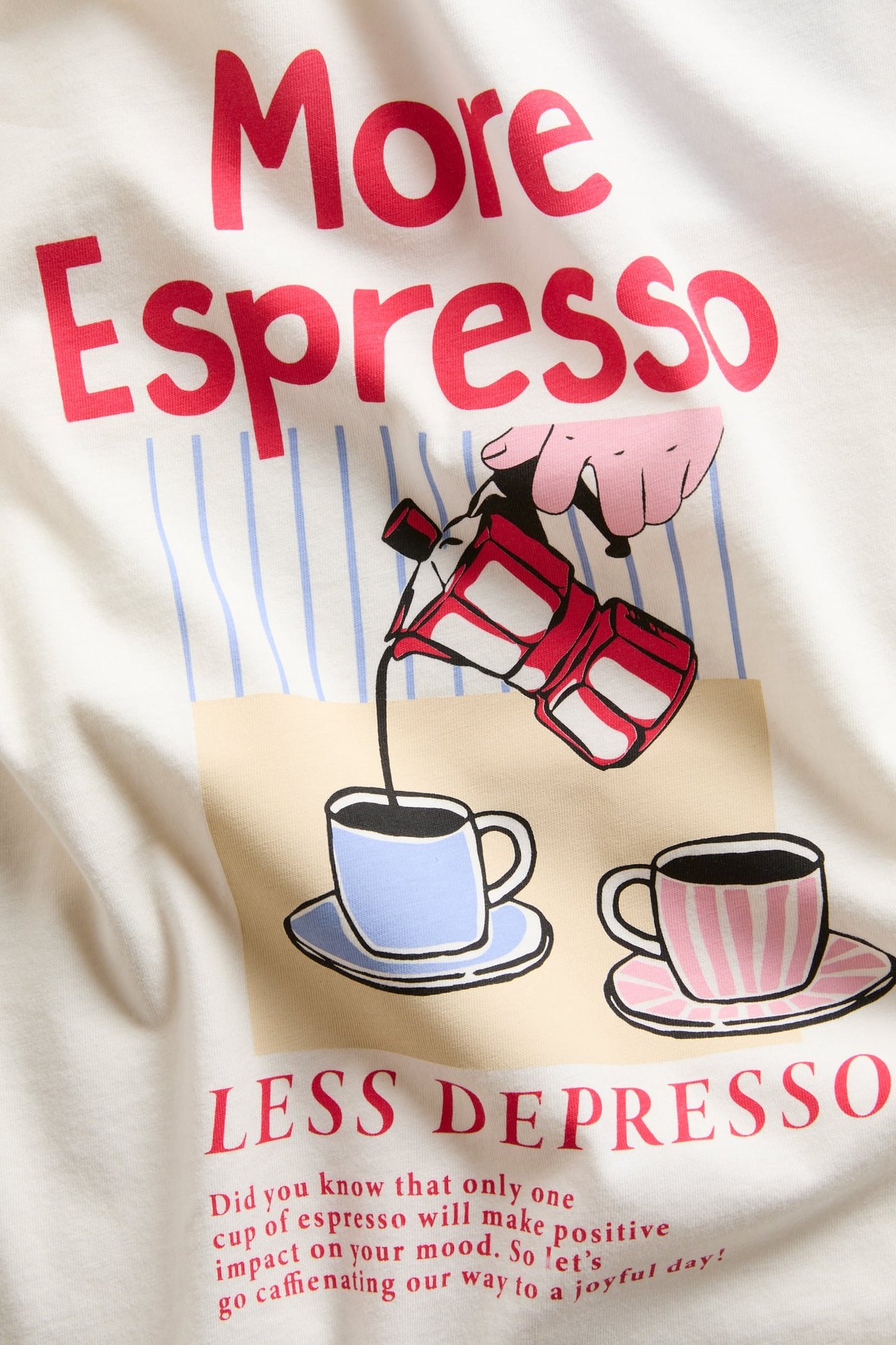Närbild av en vit t-shirt i bomull med fronttryck av texten 'More Espresso' och kaffekoppar.