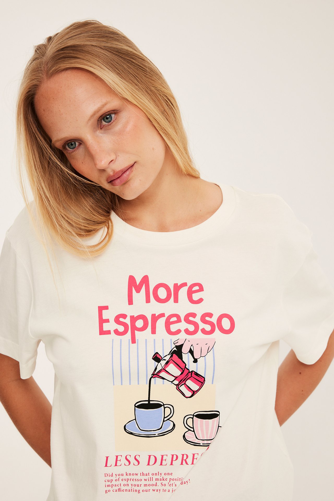 Edestä: Nainen valkoisessa puuvilla-T-paidassa, jossa vaaleanpunainen "More Espresso" -kuvio edessä.