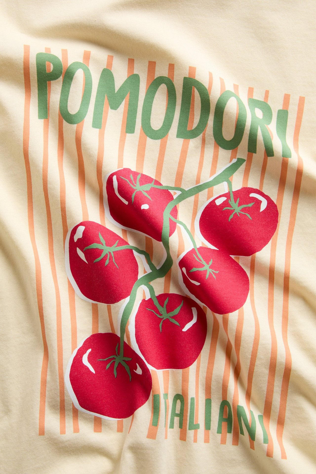 Närbild av en ljusgul t-shirt i bomull med tryck av "POMODORI" text och röda tomater.