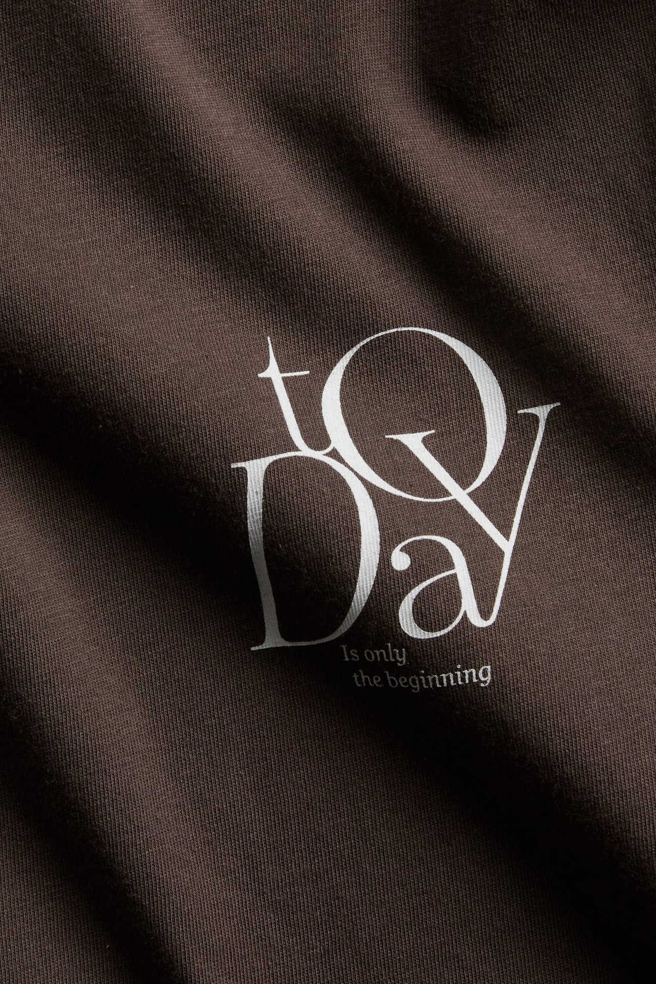 Närbild på mörkbrun bomulls-t-shirt med vitt texttryck "Today is only the beginning".