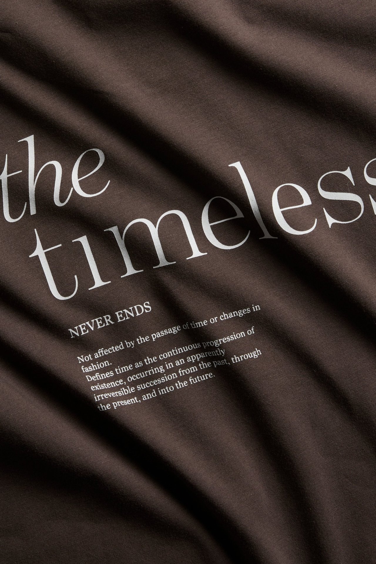 Närbild av en mörkbrun bomulls-t-shirt med vitt 'the timeless' texttryck.