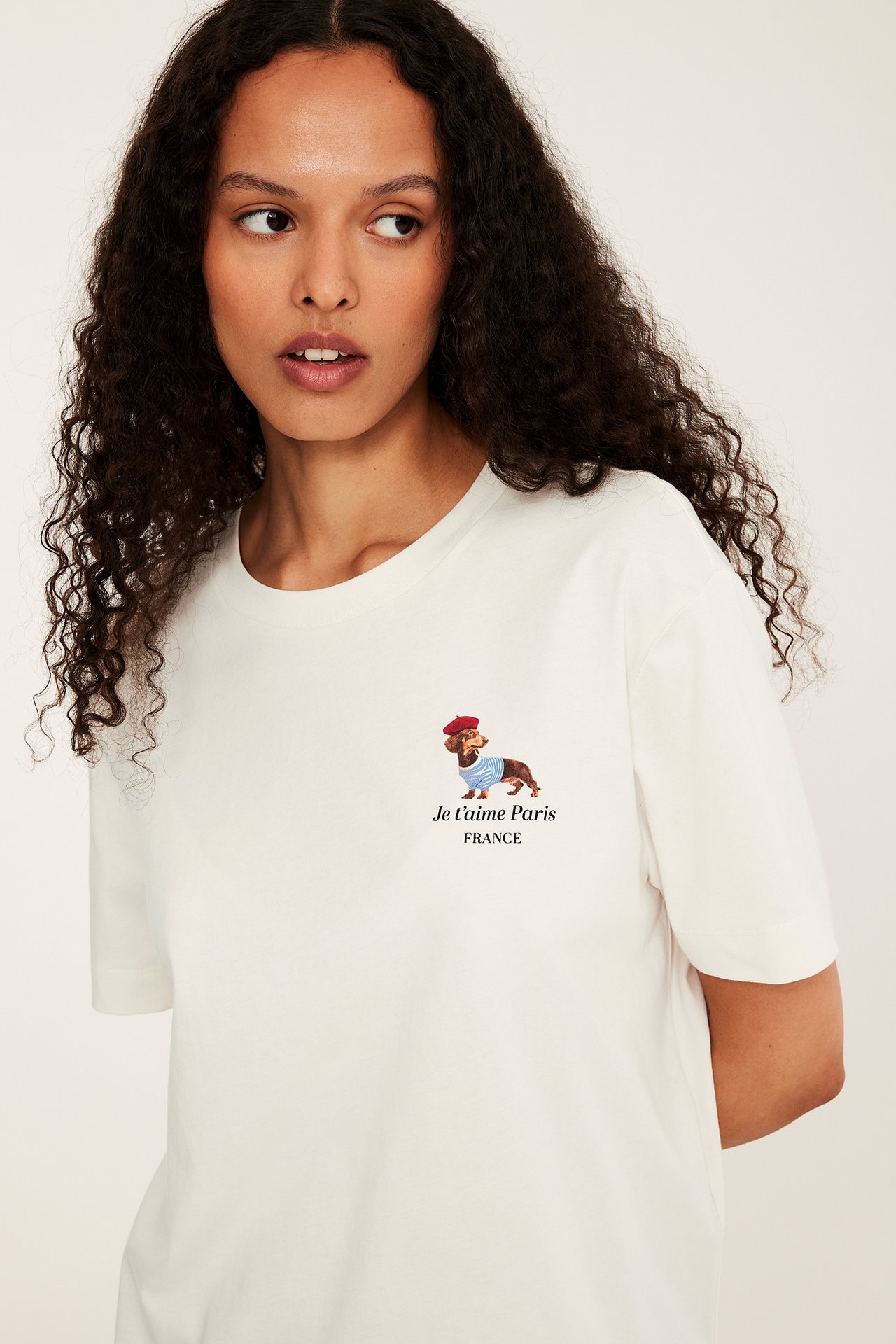 Framifrån en kvinna i en vit t-shirt av bomull med "Je t'aime Paris" tax-tryck.