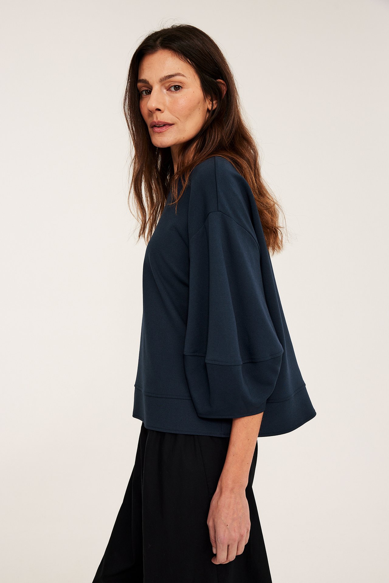 Sidovy av en kvinna i en mörkblå lös punto-topp med puffärm och svarta byxor.