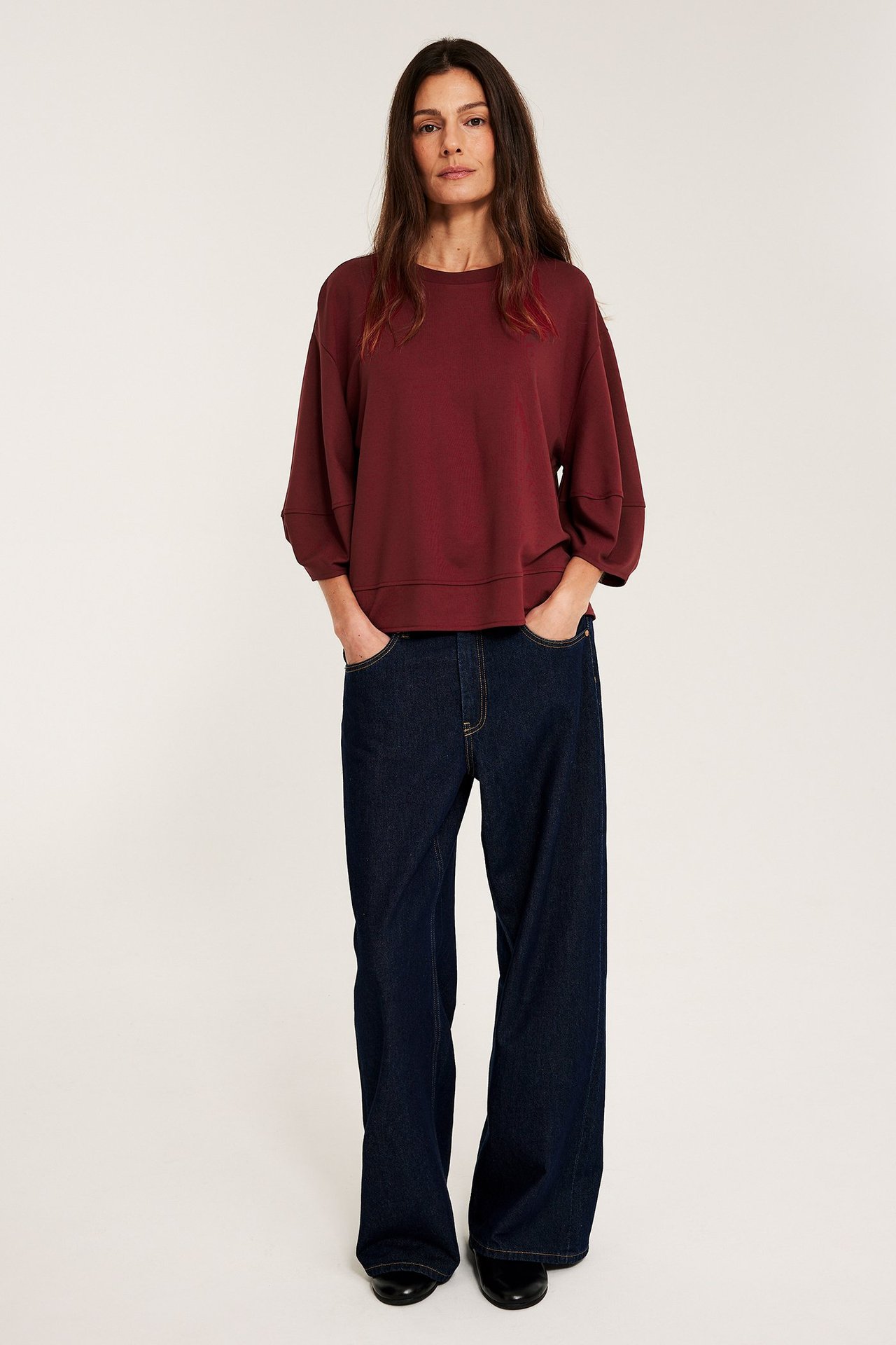 Kobieta nosi czerwoną luźną bluzkę z bufiastymi rękawami, ciemne jeansy i czarne buty.