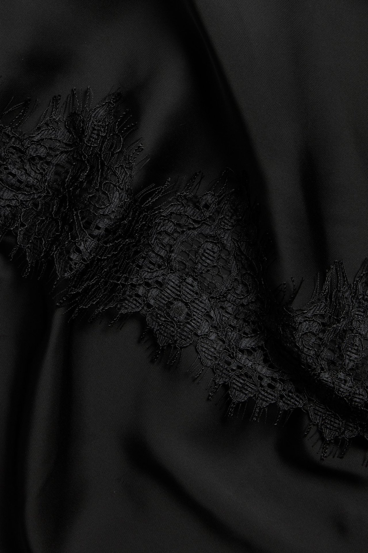Lähikuva mustasta satiinihameesta, jossa on monimutkainen musta pitsireuna.