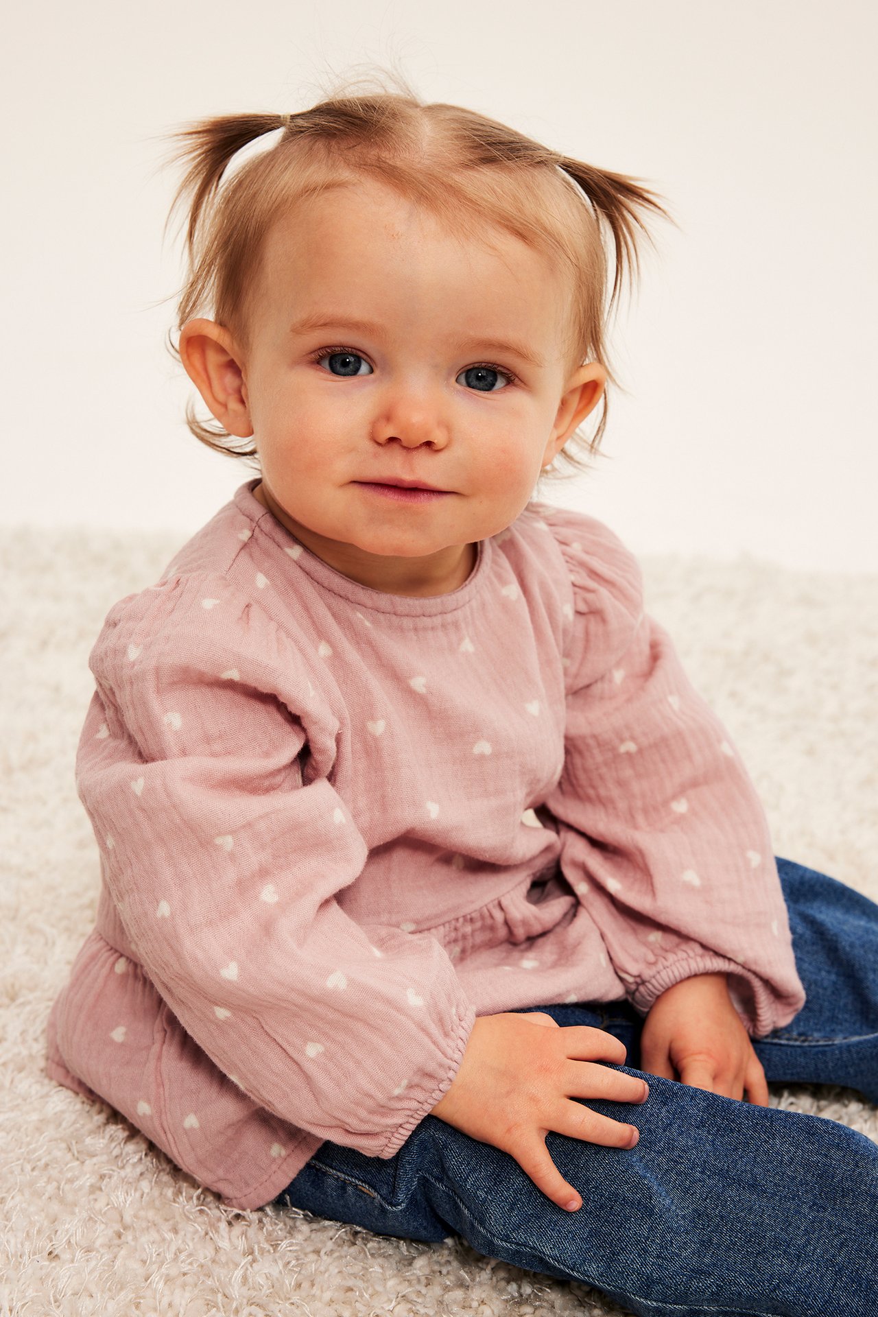 Frontbilde av baby med rosa langermet bluse med hjertemønster og blå jeans.