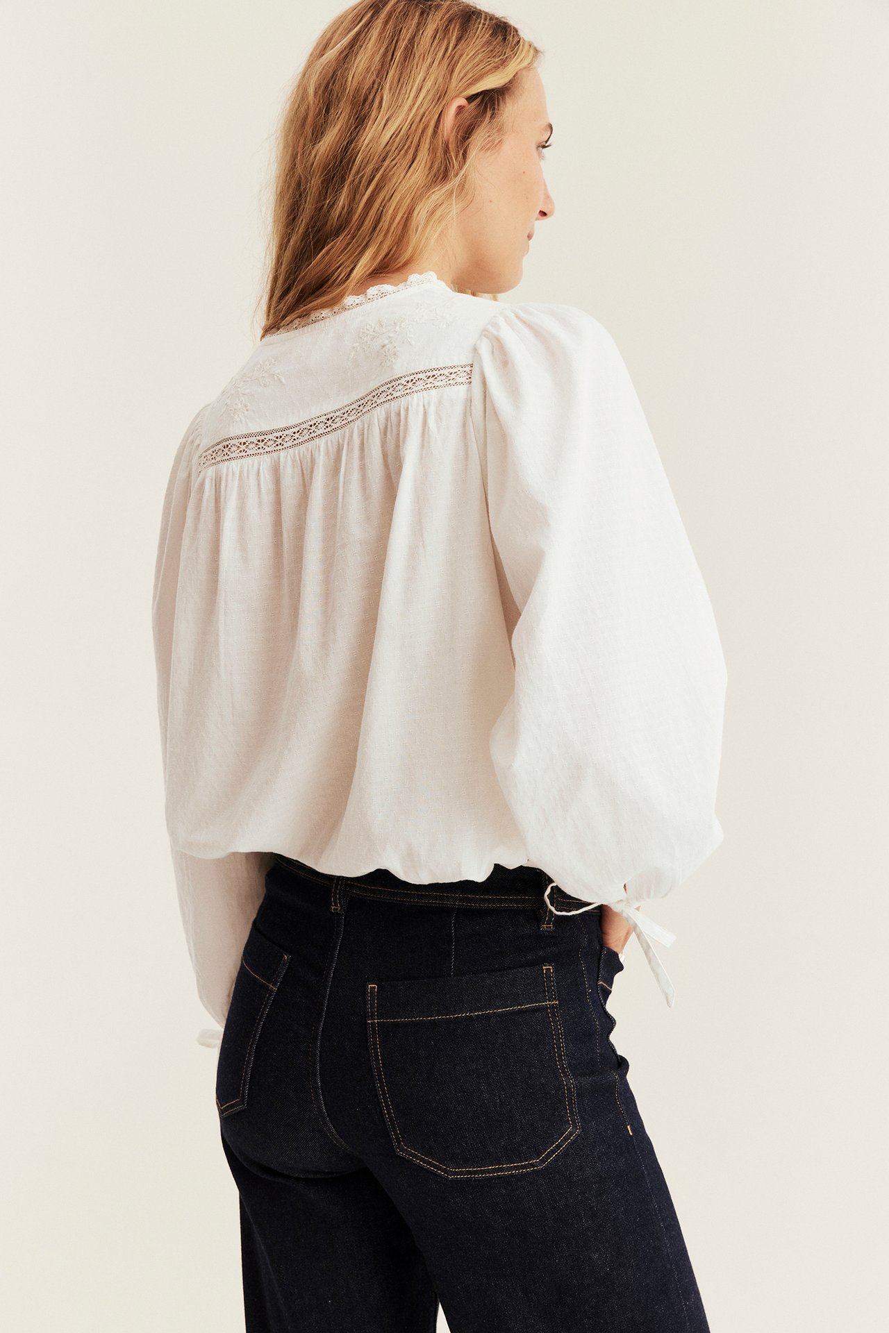 Ryggbilde av kvinnelig modell i en hvit løstsittende brodert bluse med mørkeblå jeans.