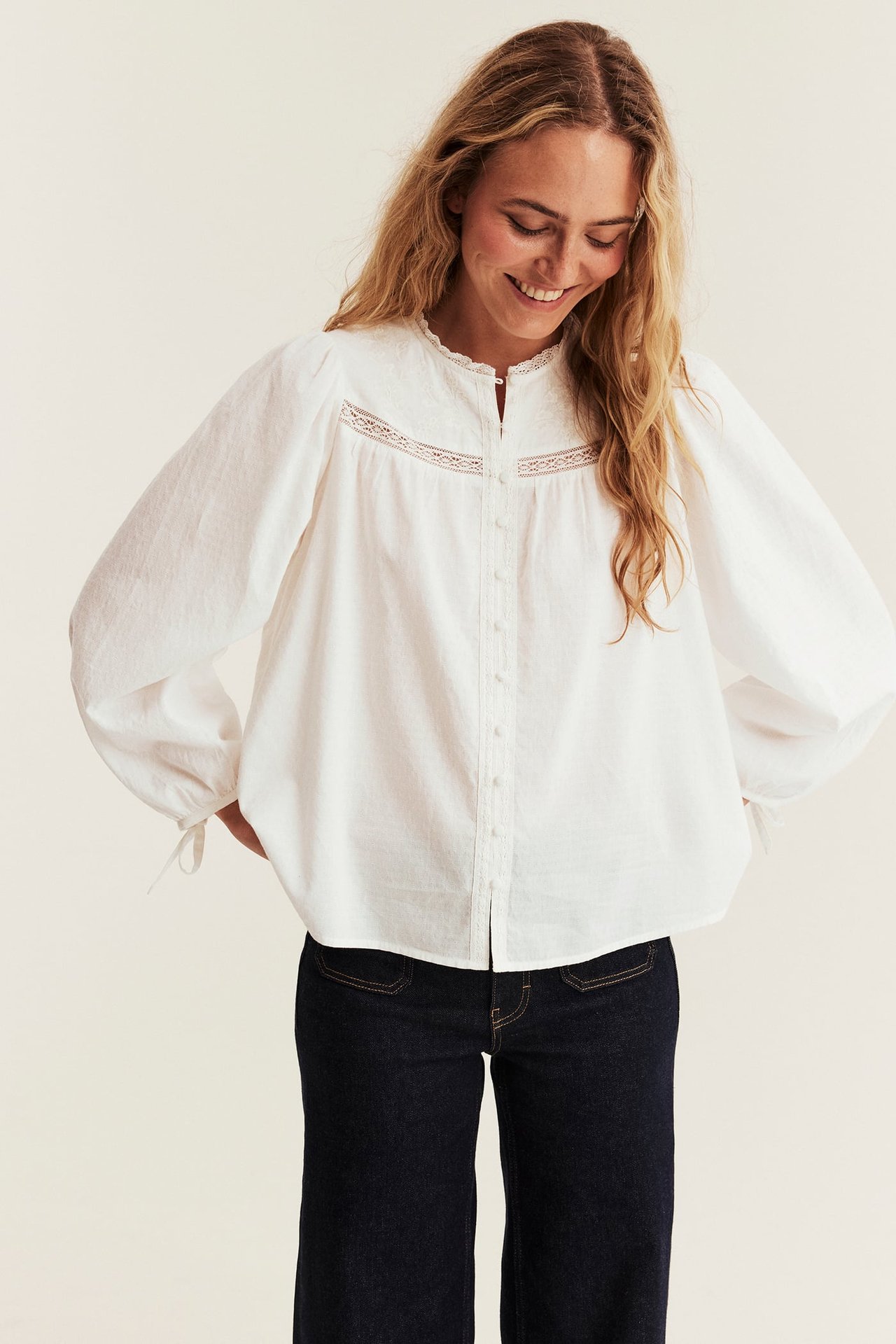 Forfra, kvinnelig modell i en hvit blondebluse og mørkeblå vide jeans.