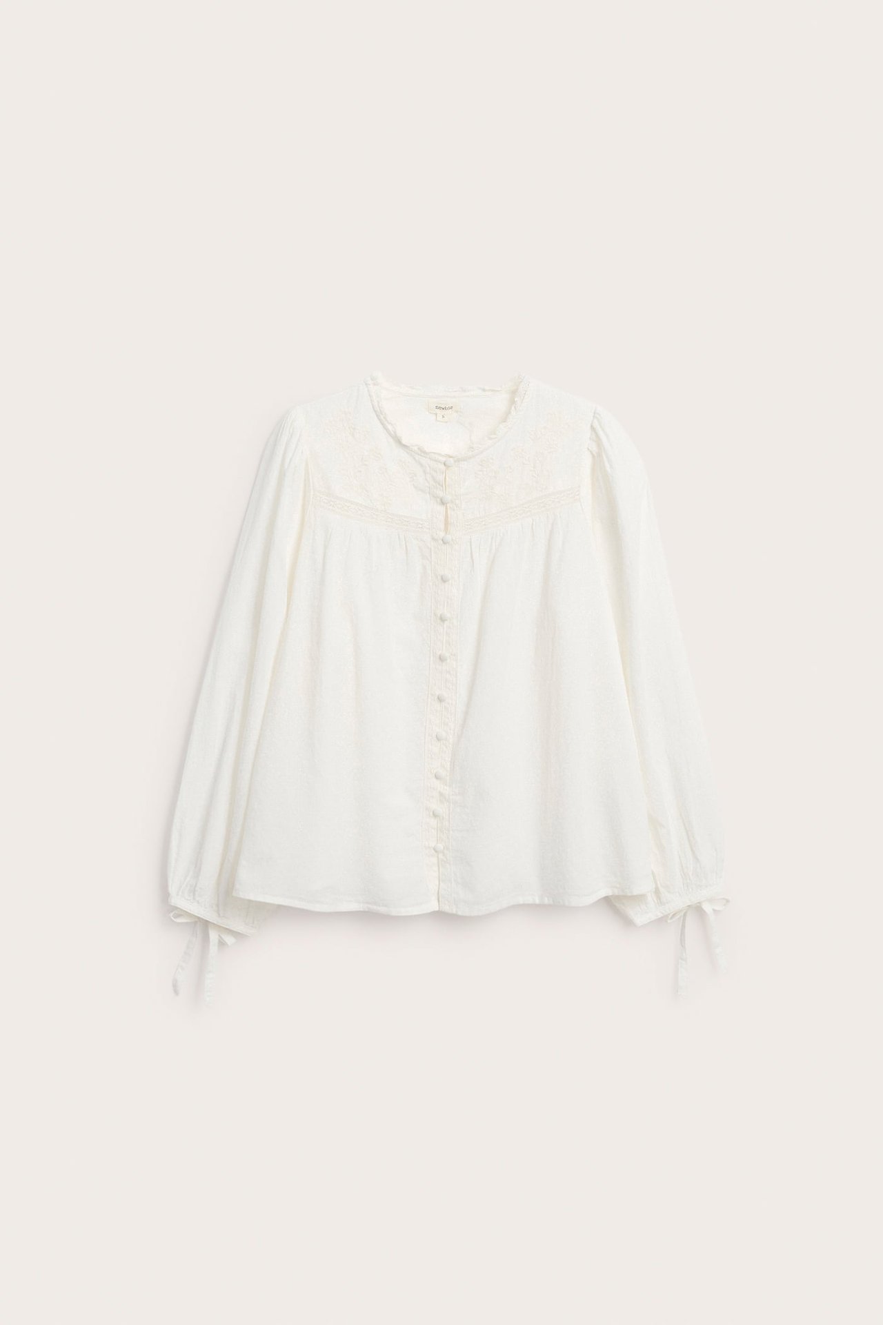 Frontvisning av en hvit langermet brodert bluse med knapper foran og knyting ved mansjettene.