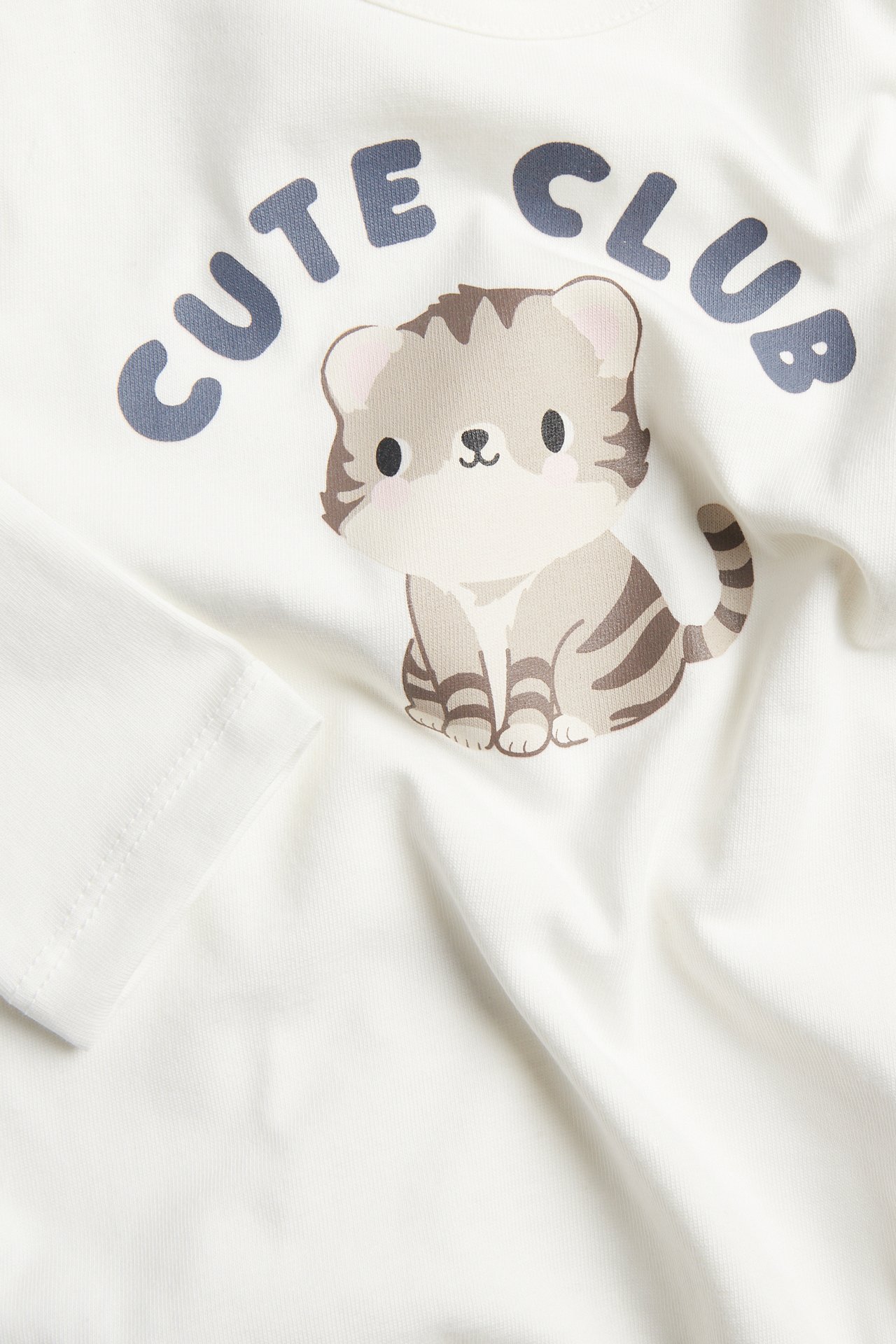 Zbliżenie na biały top z uroczą grafiką kota i napisem 'CUTE CLUB'.