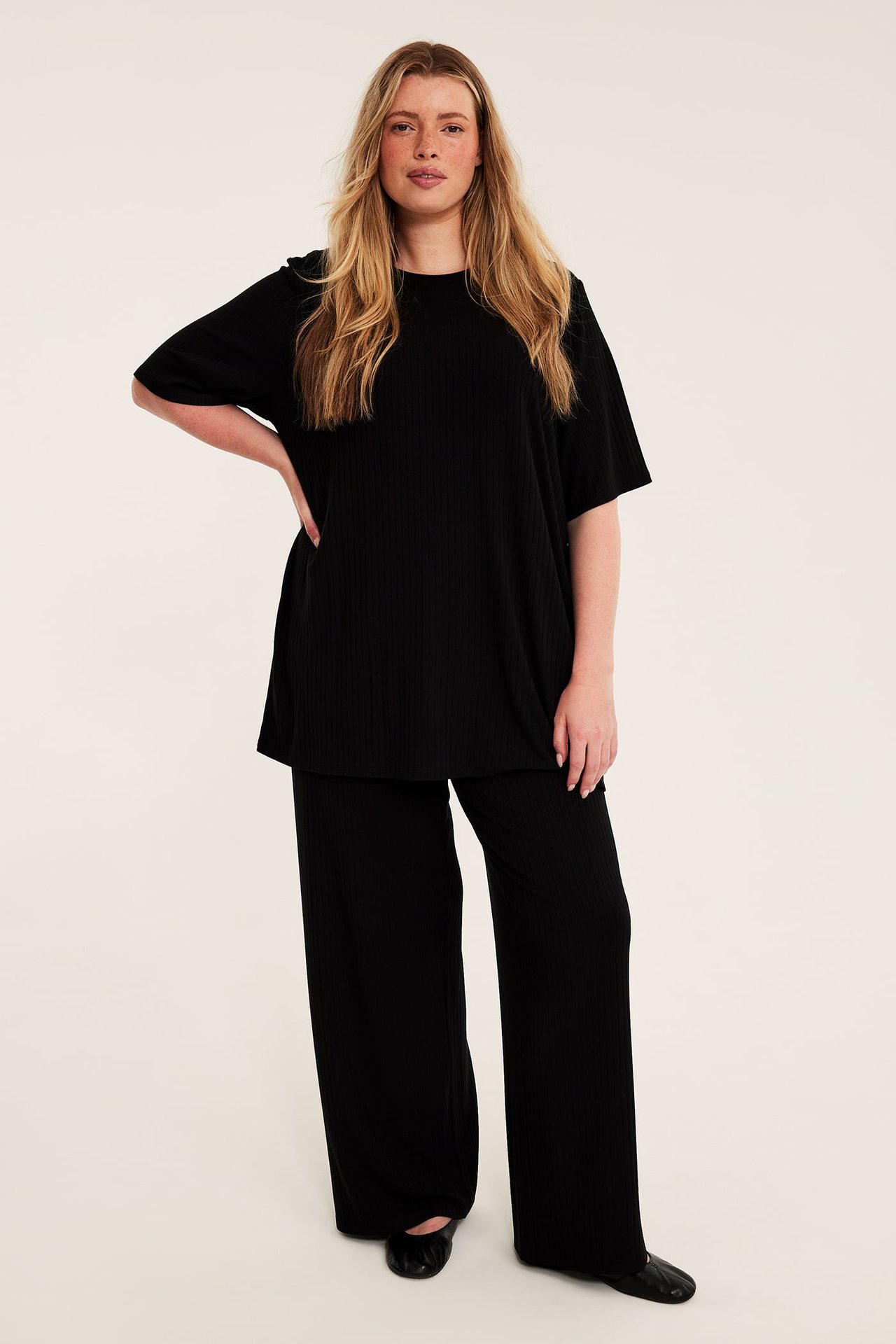 Framifrån, vuxen kvinna i svart ribbad oversize t-shirt och matchande vida byxor.