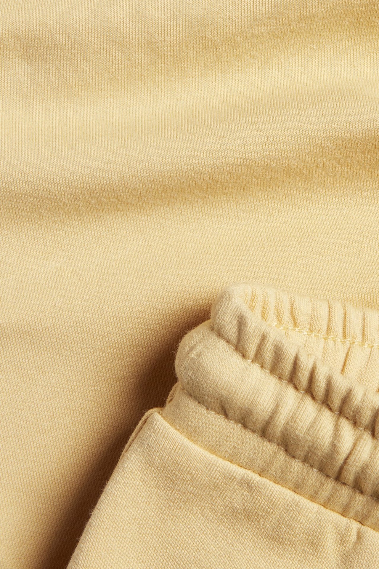 Nærbilde av lyst gult ribbet joggebuksemateriale med elastisk mansjett.
